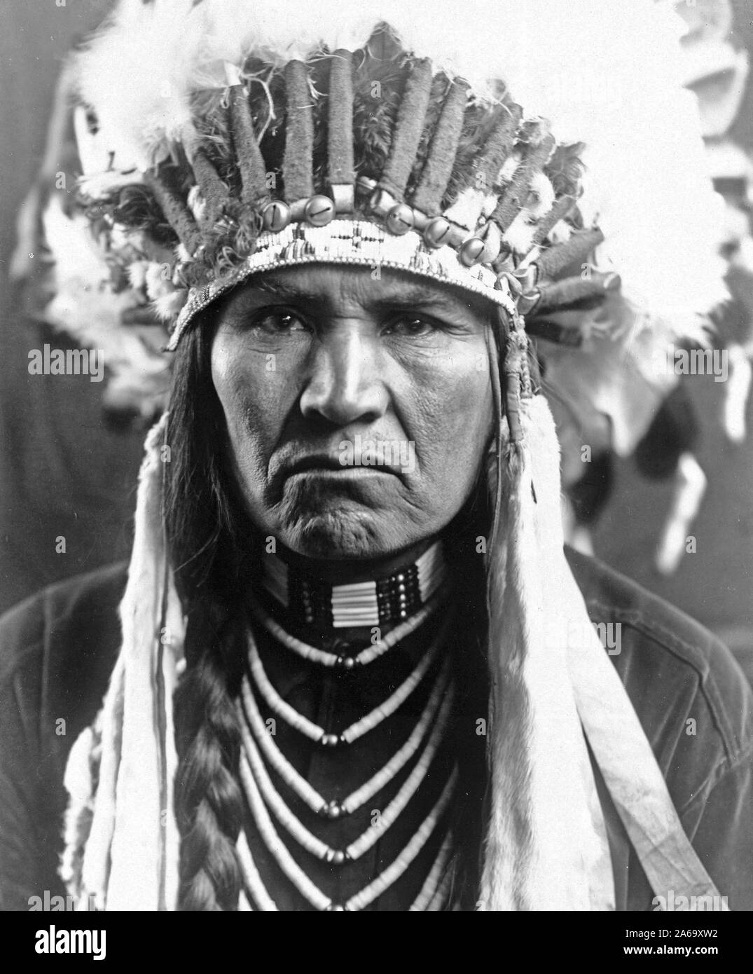 Edward S. Curtis Native American Indians - Nez Percé Mann in voller Federkopfschmuck, geflochtene Haare, und Halsketten Ca. 1910 Stockfoto