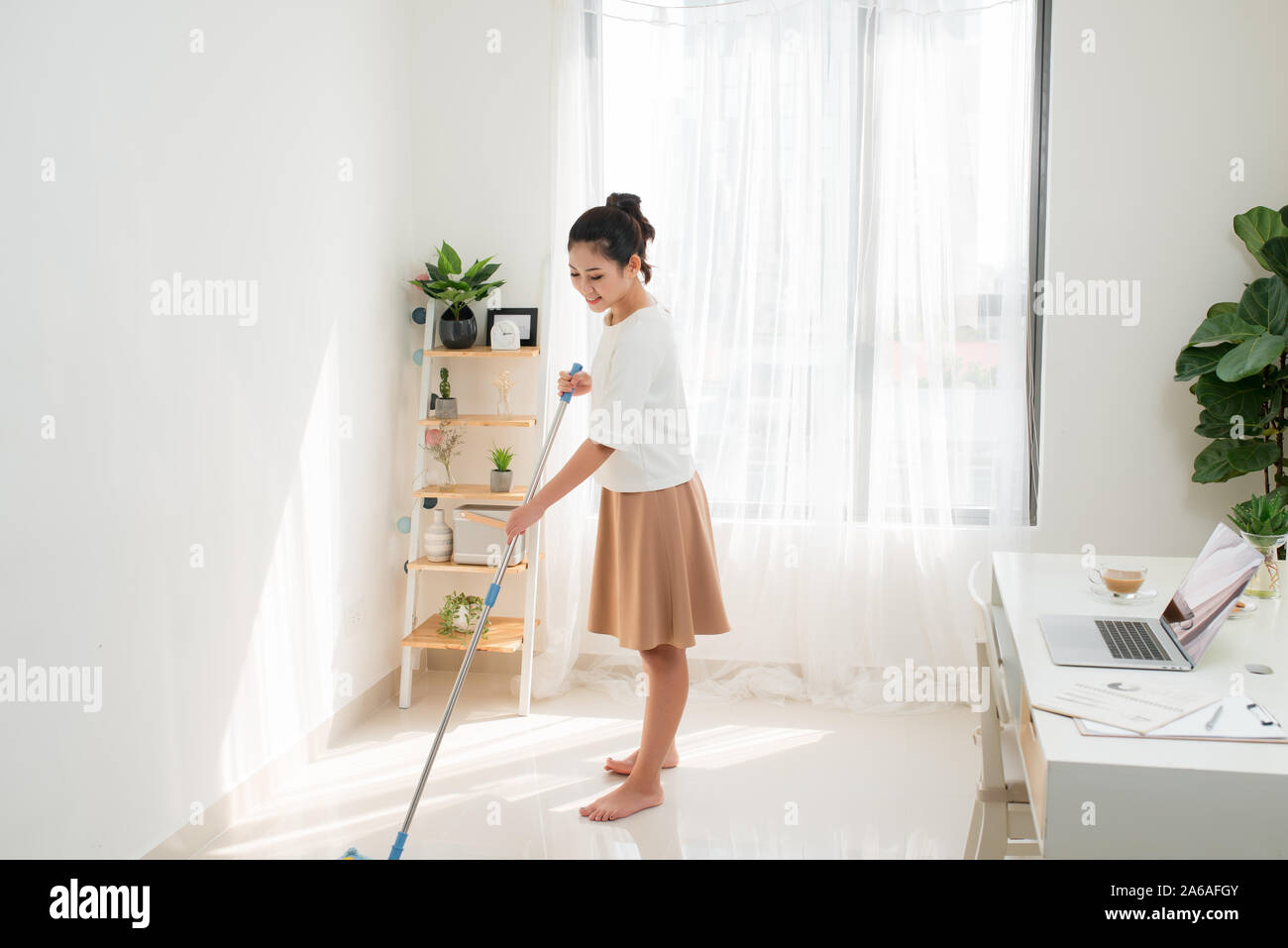 Junge asiatische Frau Reinigung Boden zu Hause chores mit attraktiven Lächeln im Gesicht. Stockfoto