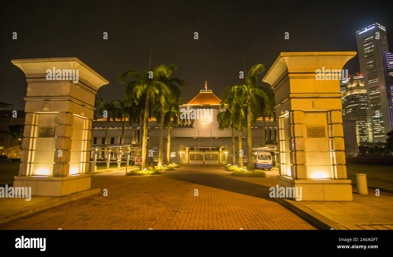 Die Singapur Parlament Gebäude mit einem Wolkenkratzer im Hintergrund bei Nacht Stockfoto