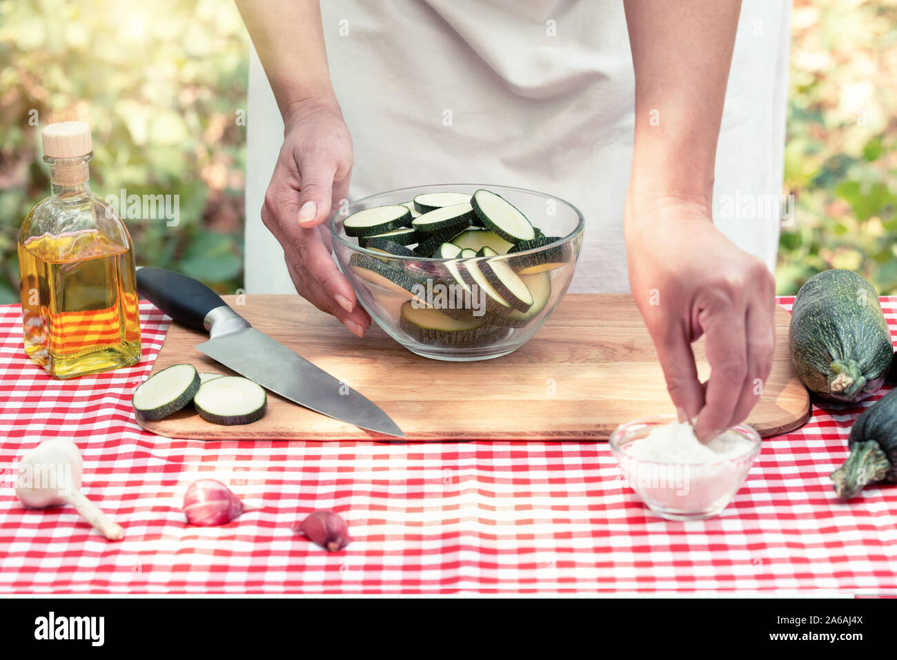 Frau Koch Salz geschnittene Zucchini. Karierte Tischdecke auf dem Tisch, natürlichen, grünen Hintergrund. Das Konzept des Kochens natürlichen umweltfreundlichen Gerichte Stockfoto
