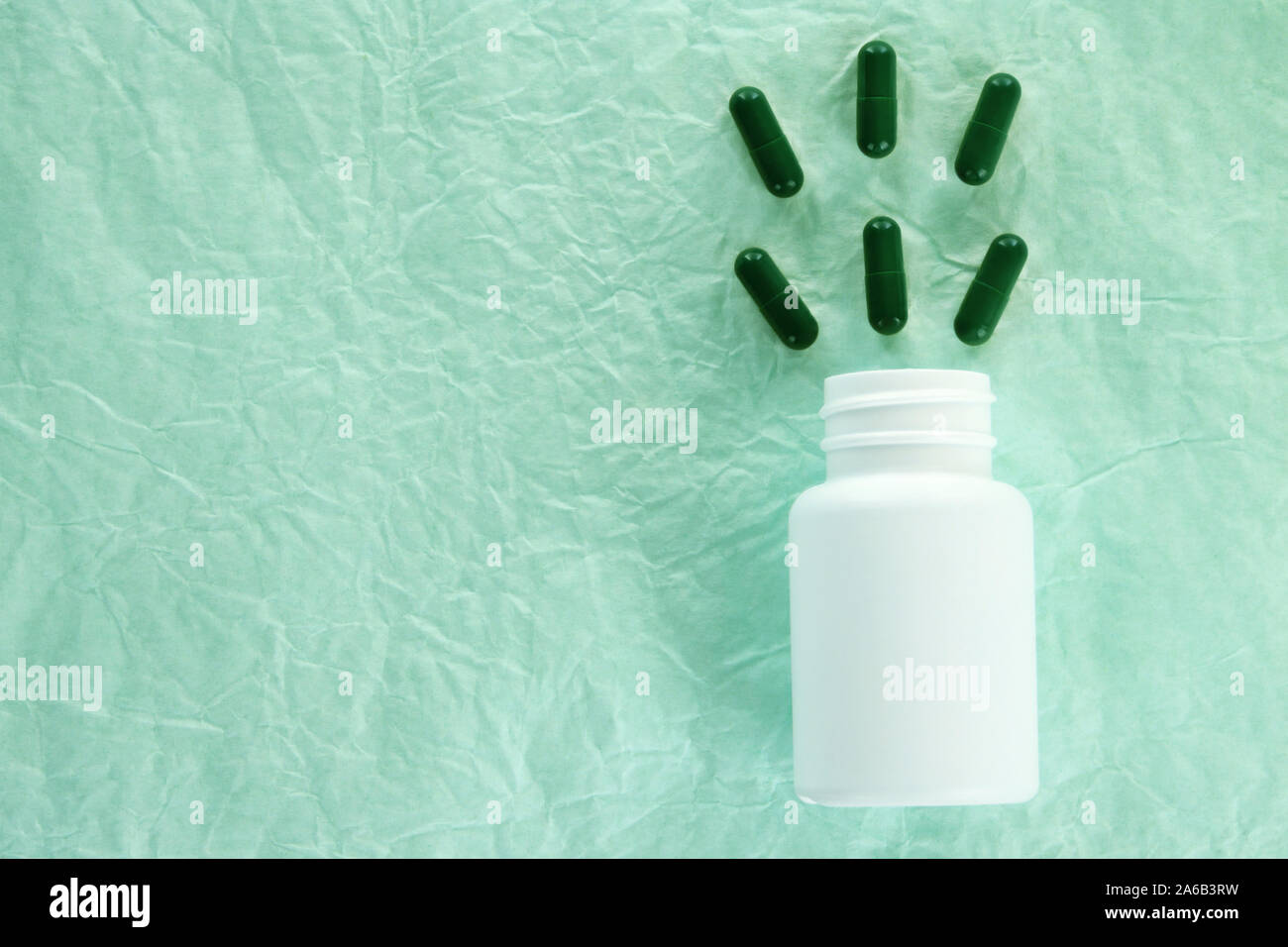 Flach Zusammensetzung mit grünen Pillen fliegen in weiße Flasche auf Türkis zerknittertes Papier Hintergrund Stockfoto