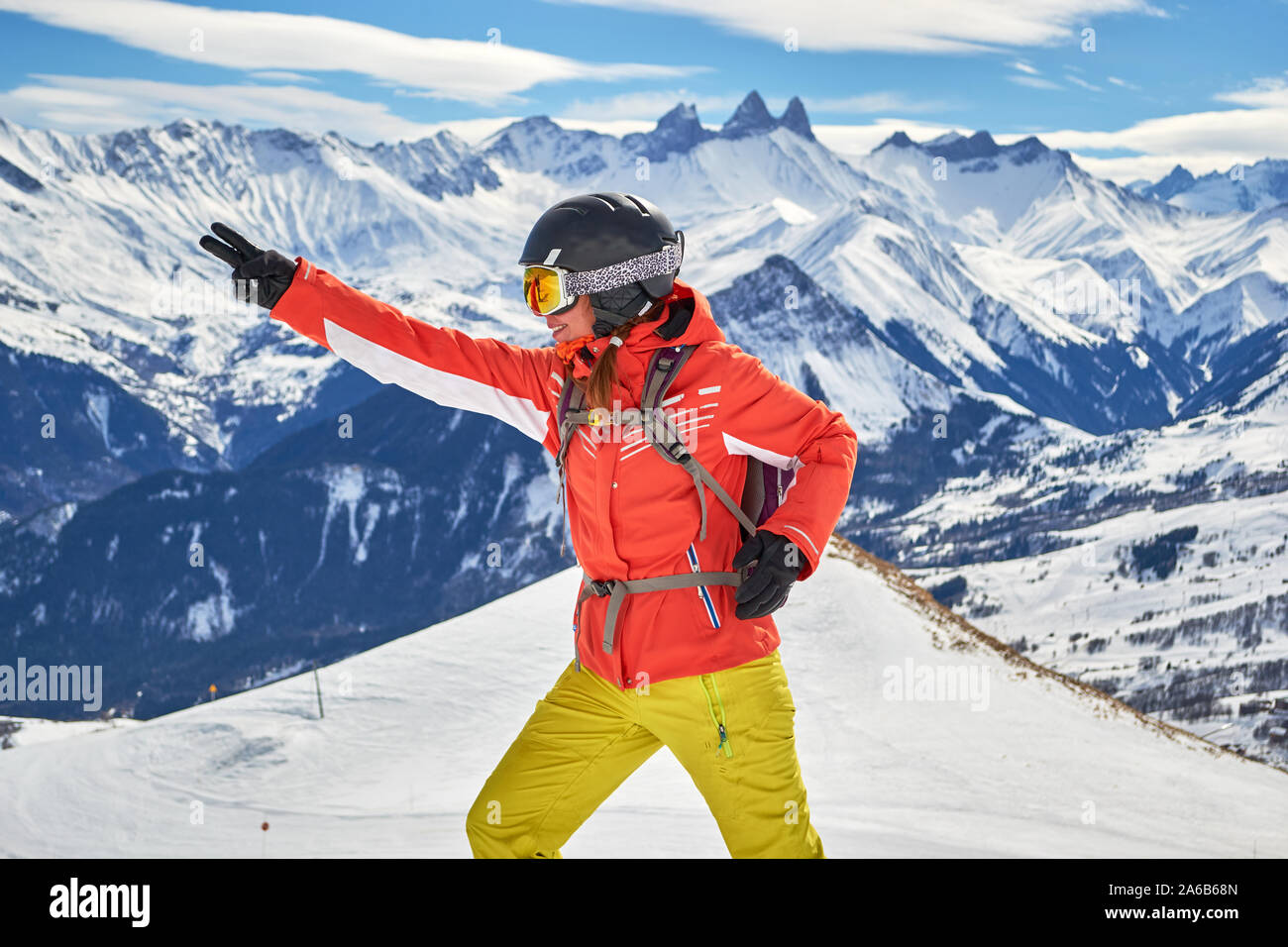 Frau Skifahrer lächelnd und im Les Sybelles Skigebiet posiert, mit Aiguilles d'Arves Gipfeln im Hintergrund, an einem sonnigen Tag mit blauem Himmel. Stockfoto