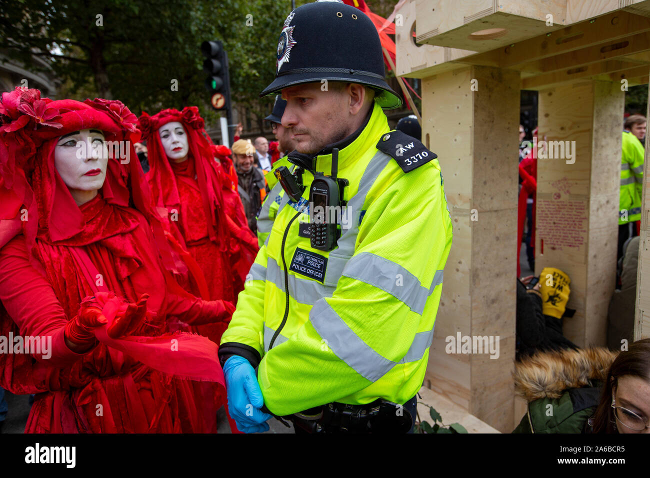 London, 10. Oktober 2019, vom Aussterben Rebellion Gruppe in rot Kostüme surround Polizei acivists vorbereiten, die sich um eine Holz- struktur in der Straße neben dem Trafalgar Square gesperrt haben zu verhaften. Stockfoto