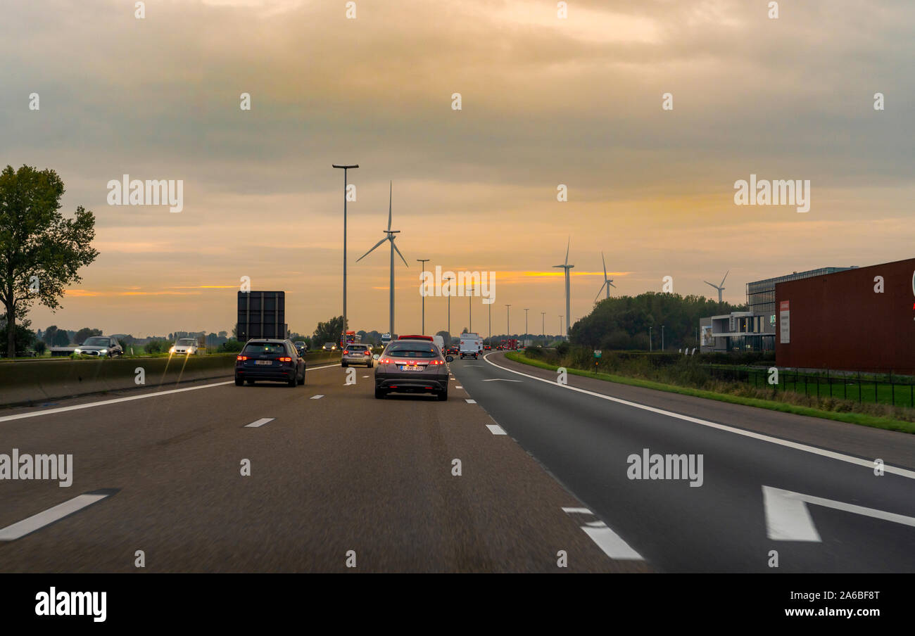 Antwerpen/Belgien - 07 Oktober 2019: Die goldenen Himmel scheint und Auto läuft in die Richtung der Golden Sky mit Windenergie Tribune. Stockfoto