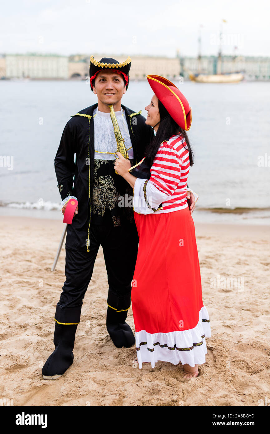 Junge glücklich kaukasische Frau in Piraten Kostüm eine Pistole an den lächelnden Mann auf Sandstrand. Vertikale. Stockfoto