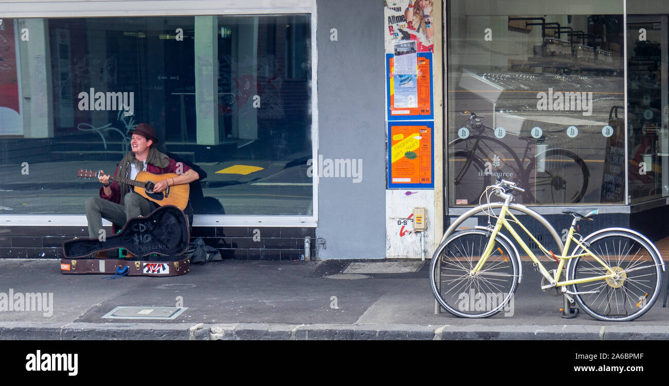 Kaukasische männlichen Gaukler spielen eine akustische Gitarre auf Smith St Collingwood Melbourne, Victoria, Australien. Stockfoto
