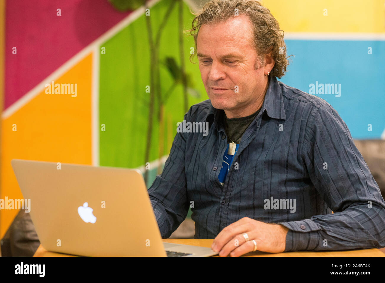 Ein Mann sitzt an einem Schreibtisch im Zimmer, der an einem Notebook arbeitet Stockfoto