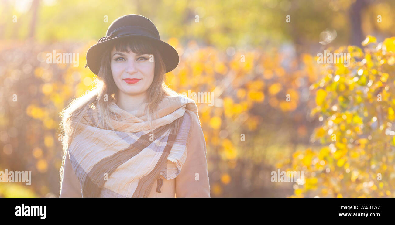 Eine hübsche Frau von 30-35 Jahre alt mit einem schönen Lächeln in einem Hut und Mantel in der Nähe von einem gelben Bush, Stockfoto