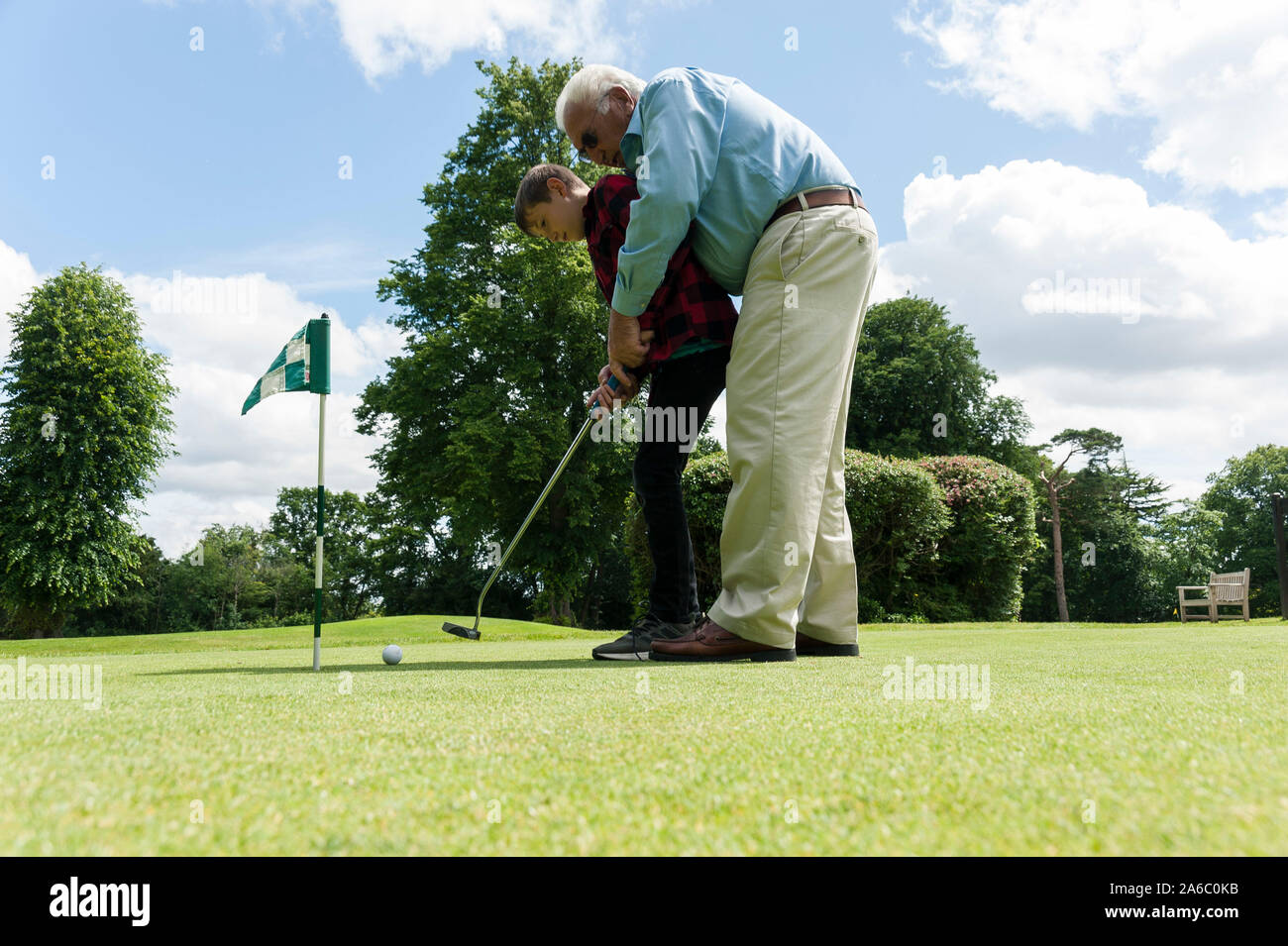 Ein Großvater lehrt seine Enkelin, wie man einen Putter auf einem Golf Putting Green verwendet. Stockfoto