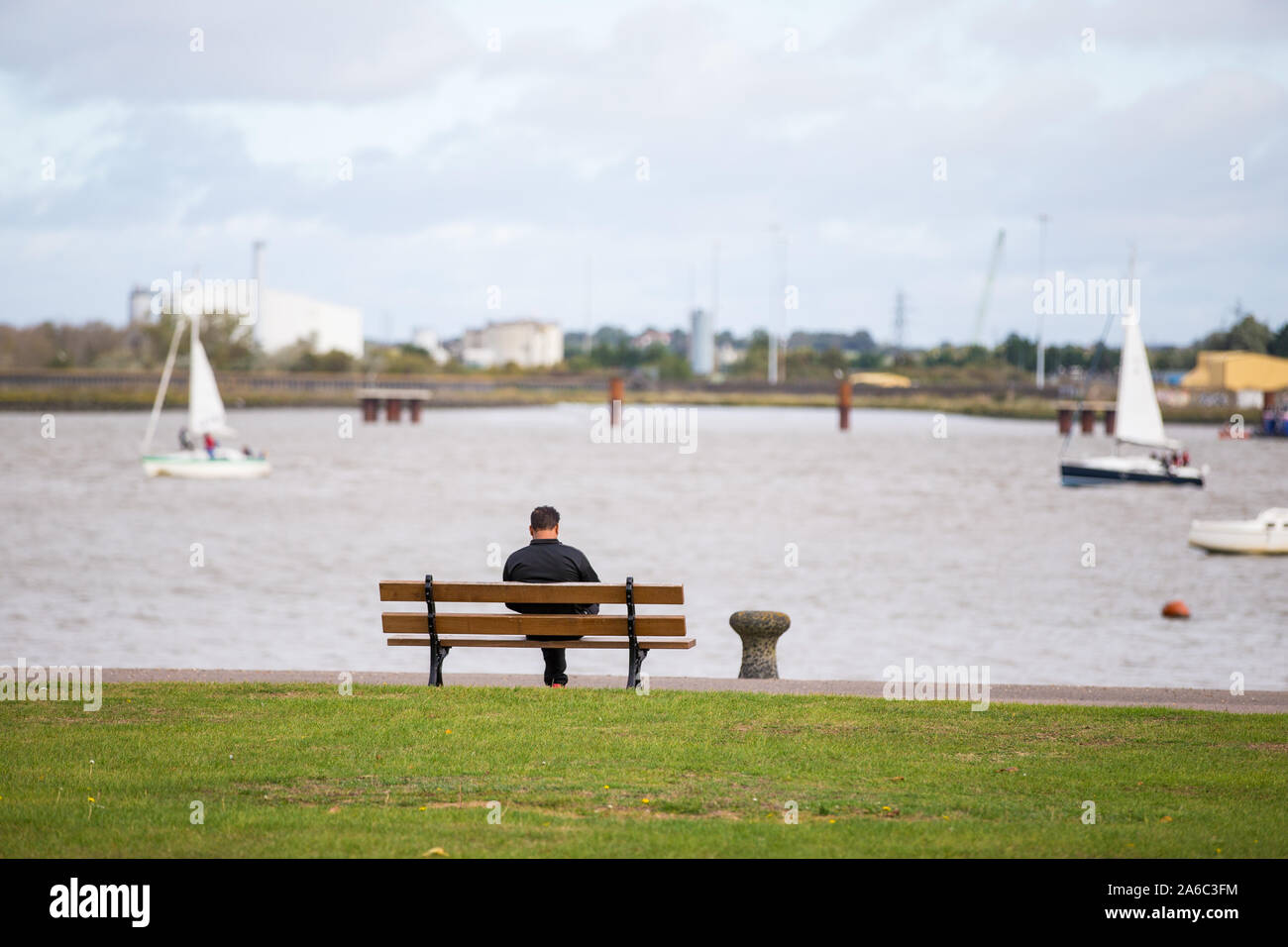 Ein Mann sitzt alleine auf einer Bank neben der Themse in Gravesend, Kent, Großbritannien Stockfoto