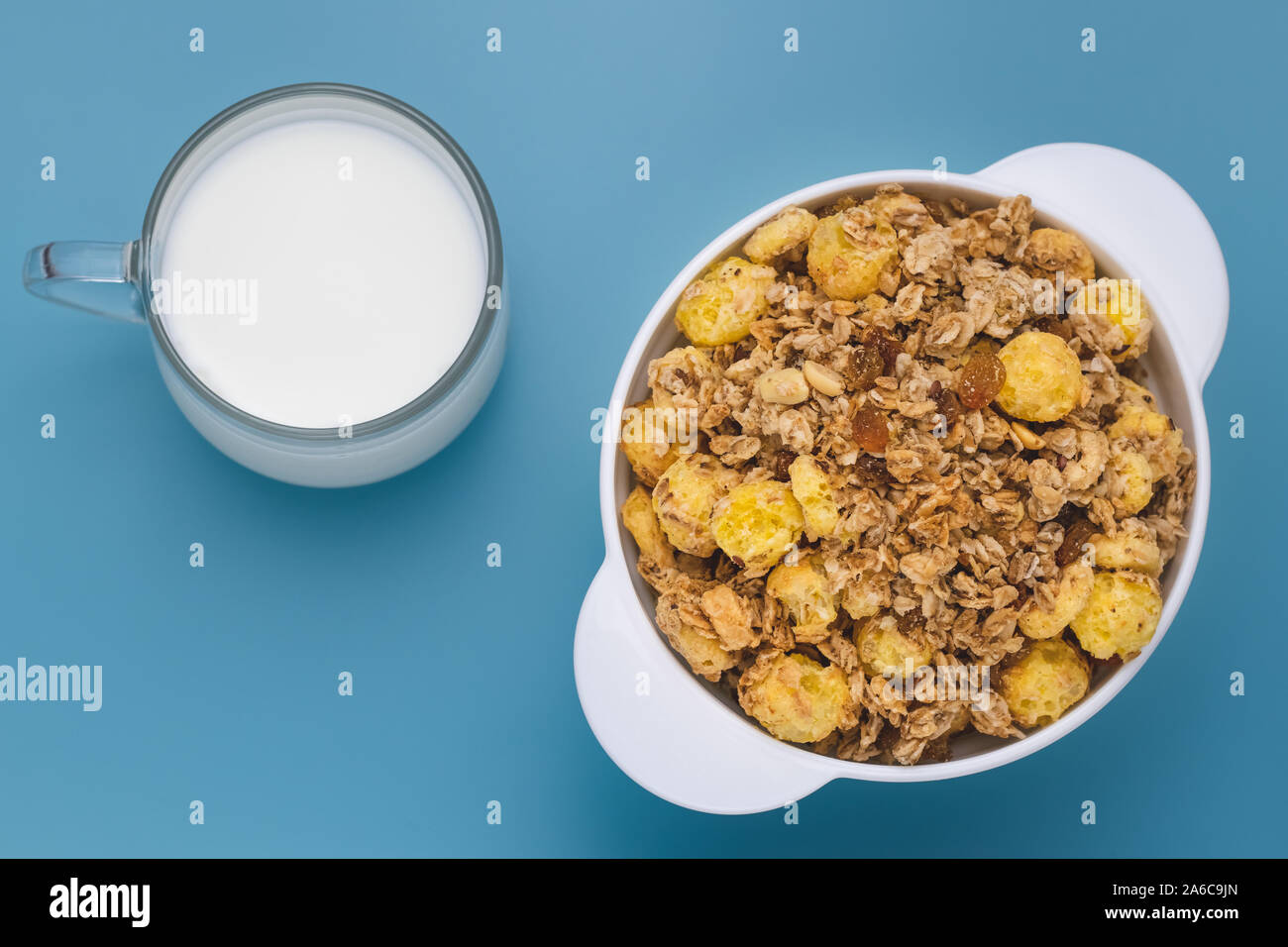 Eine Mischung von Getreide getrocknet und Muttern mit Milch zum Frühstück. Glas Tasse Milch mit Haferflocken in einer weißen Platte an der blauen Tabelle. Weiße Schüssel Müsli w Stockfoto