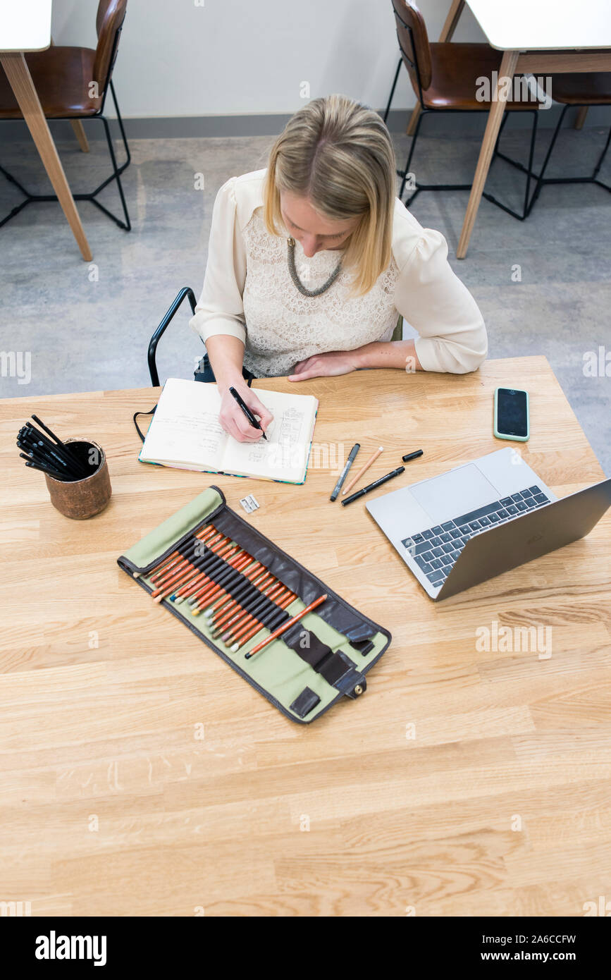 Eine Frau sitzt an einem Tisch in einem Cafe, Notizen und Skizzen in einem Notepad Stockfoto