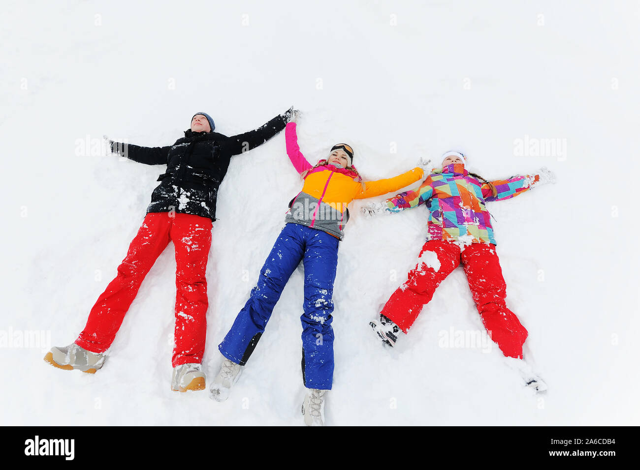 Eine junge Familie mit drei - Mutter, Vater und Tochter liegen auf dem Schnee in einem hellen Skianzuege oder im Winter Kleidung und ein Engel machen Stockfoto