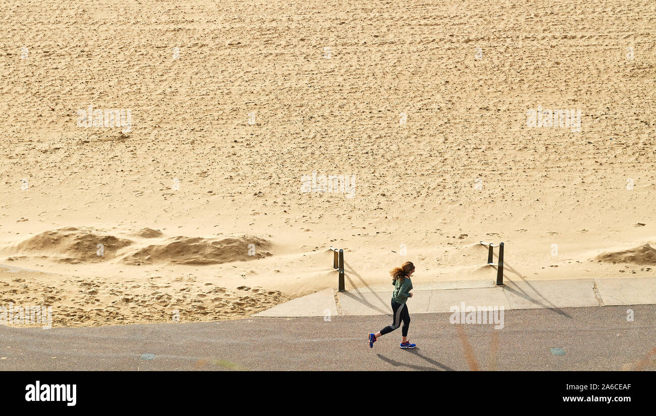 Eine Frau joggt entlang der Promenade nahe der Sandstrand in Bournemouth, England. Stockfoto