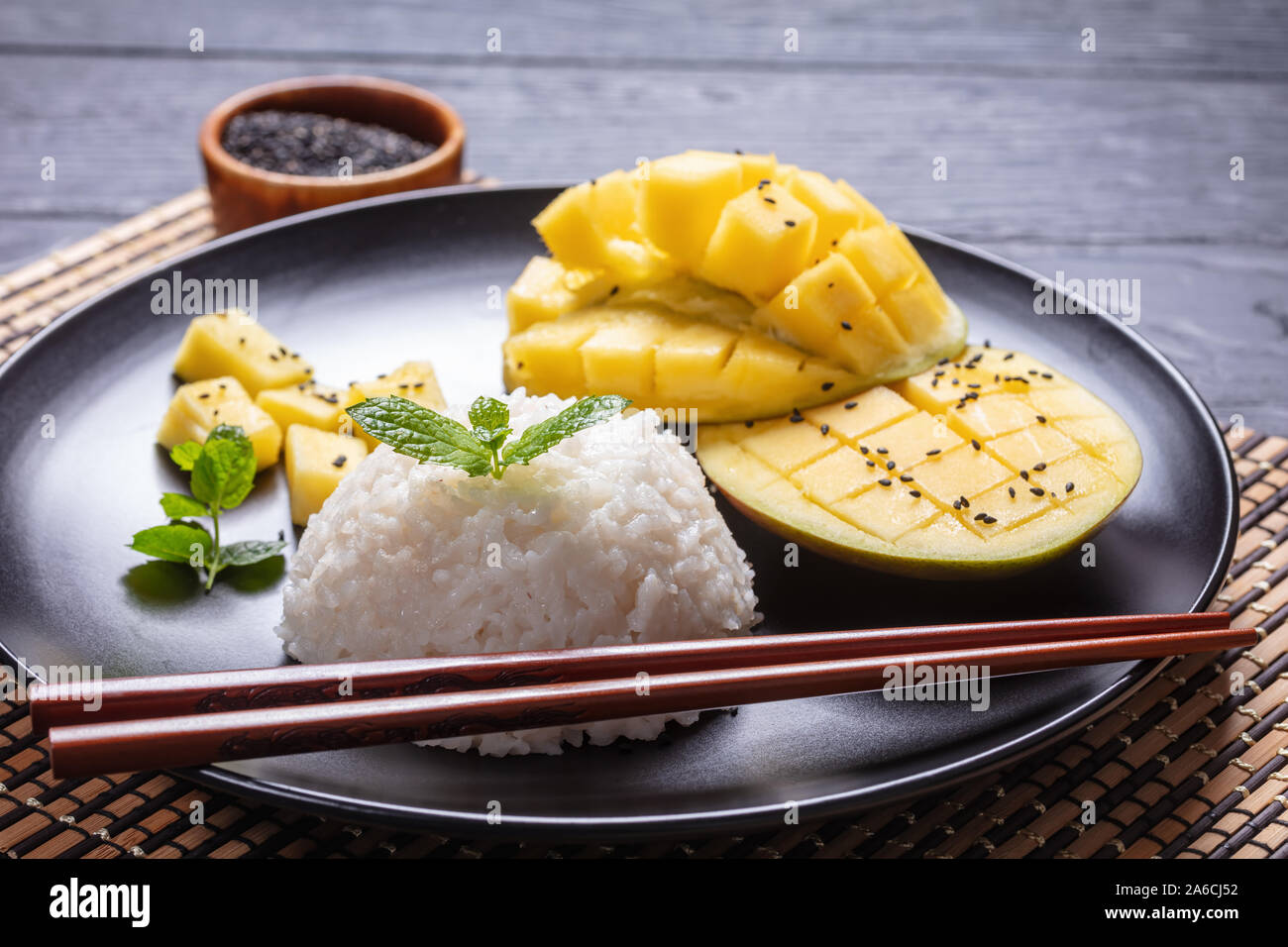 In der Nähe von Thai Dessert, cremige klebrigen Reis mit Kokosmilch gekocht und serviert mit frischen Mango auf einer schwarzen Platte mit Stäbchen Stockfoto