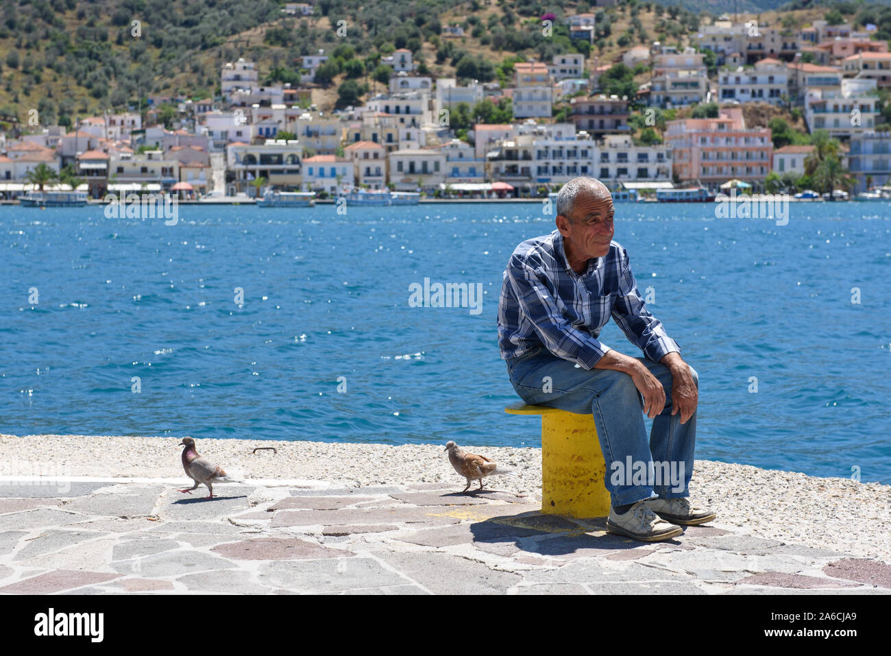 14.06.2016. POROS, Griechenland. Ein alter Mann sitzt in der Nähe der Küste und entspannend, während 2 taube vögel Wandern in der Nähe von ihm. Stockfoto