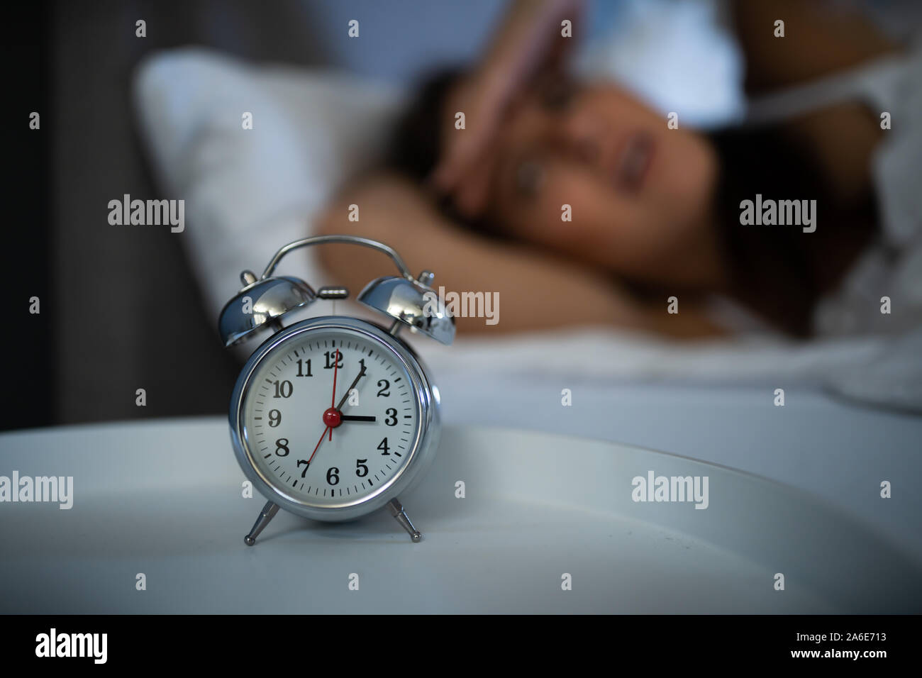 Schlaflose Frau schaut auf die Uhr mitten in der Nacht im Bett Stockfoto