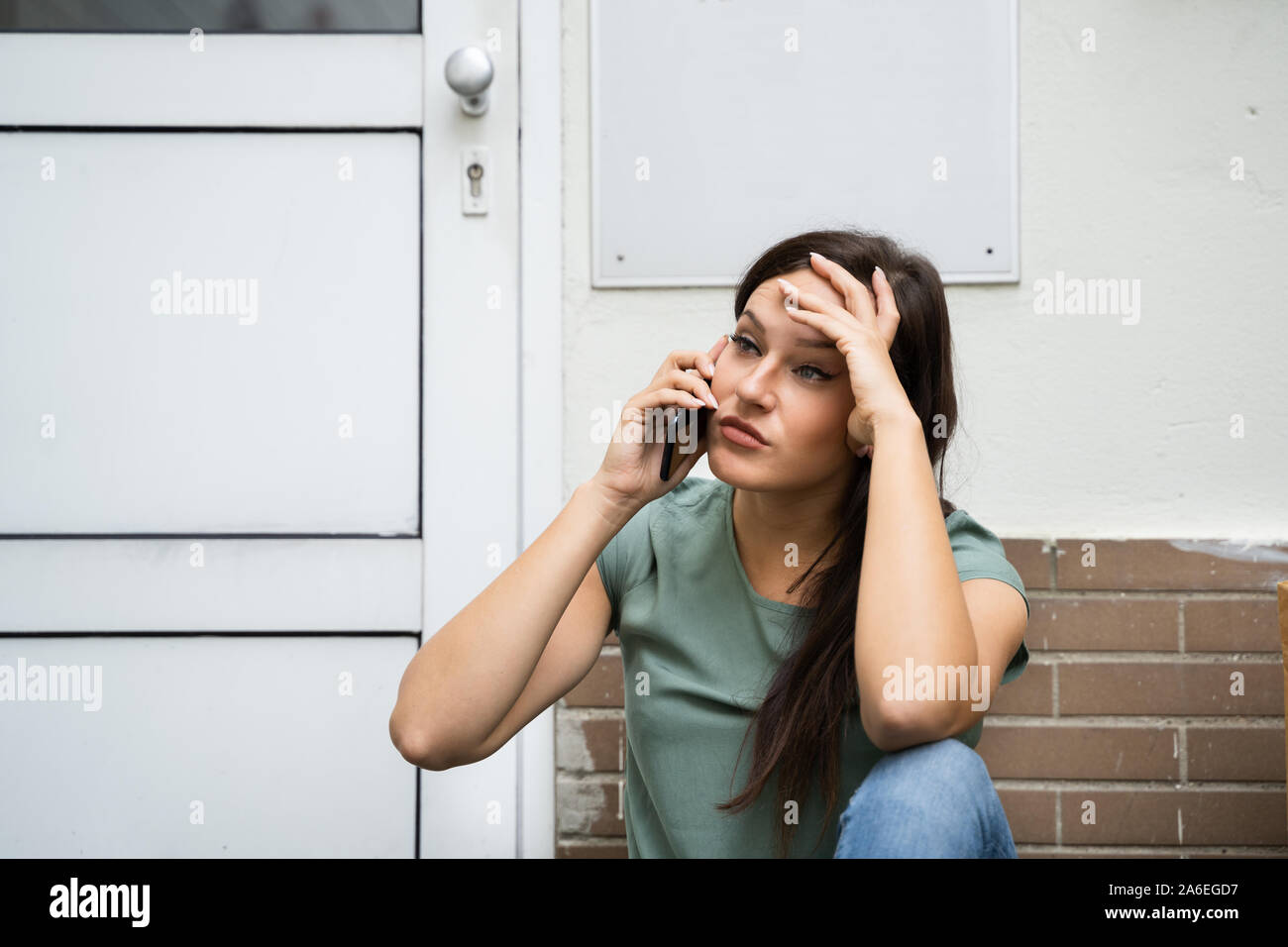 Eine Angst junge Frau sitzt vor der Tür Sprechen auf Mobilephone Stockfoto