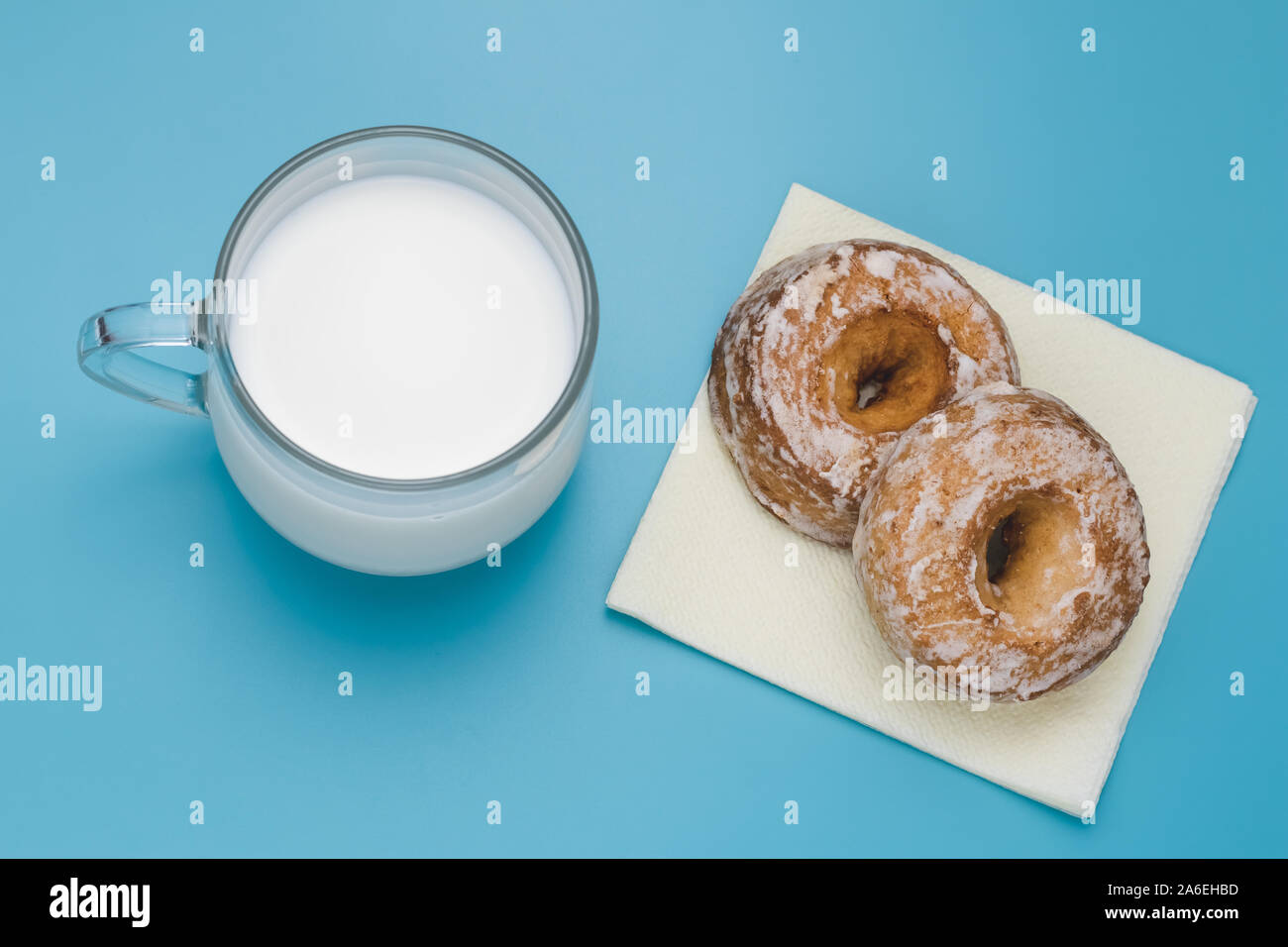 Tasse Milch und zwei Kuchen auf einem blauen Hintergrund. Frühstück Konzept. Cookies Auf gelbes Papier Serviette. Stockfoto
