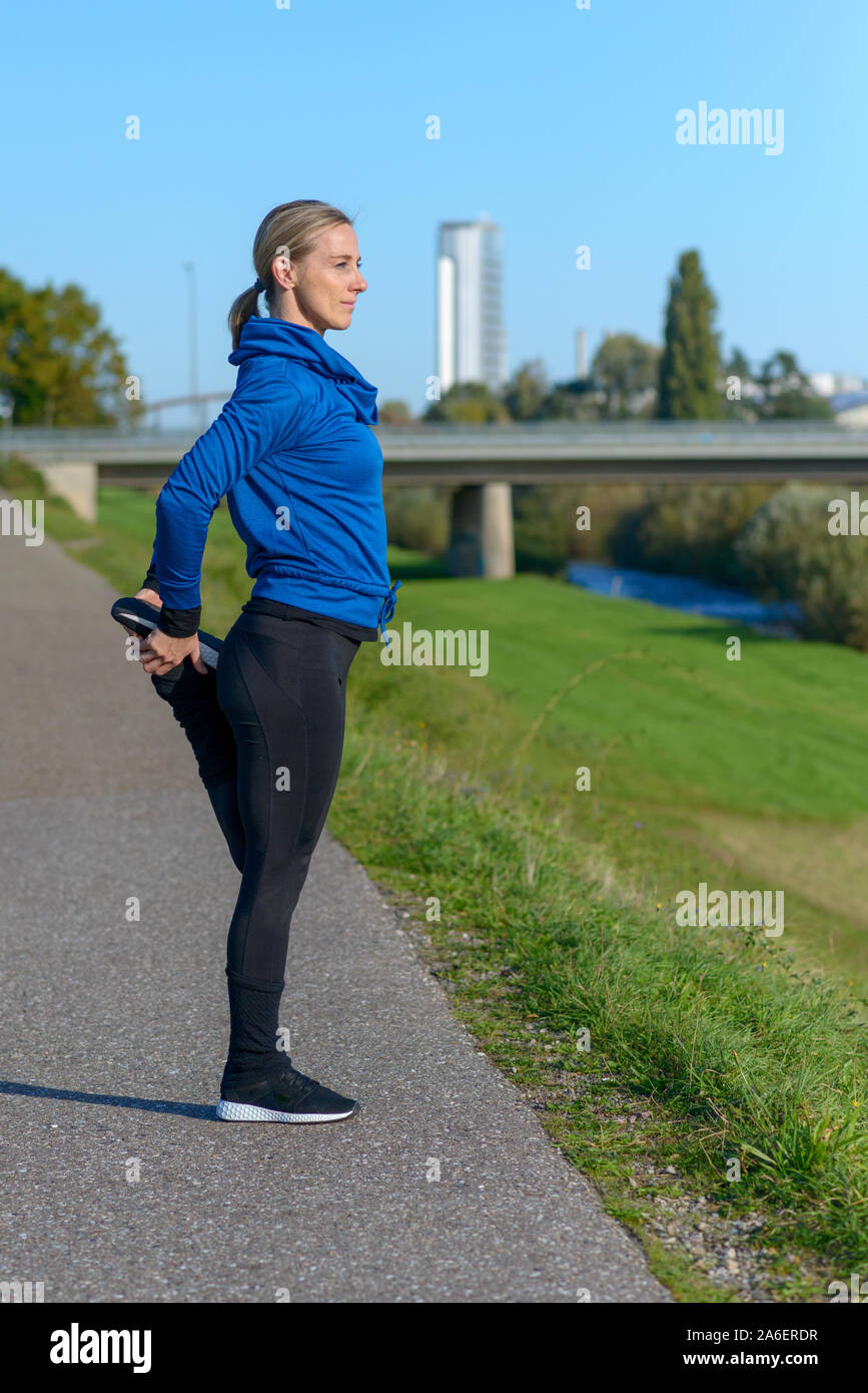 Kompromisslos sportliche Frau, die Arbeiten an einem sonnigen Wintertag auf einem Weg neben einem Fluß bis limbering tun Dehnübungen vor dem Joggen Stockfoto
