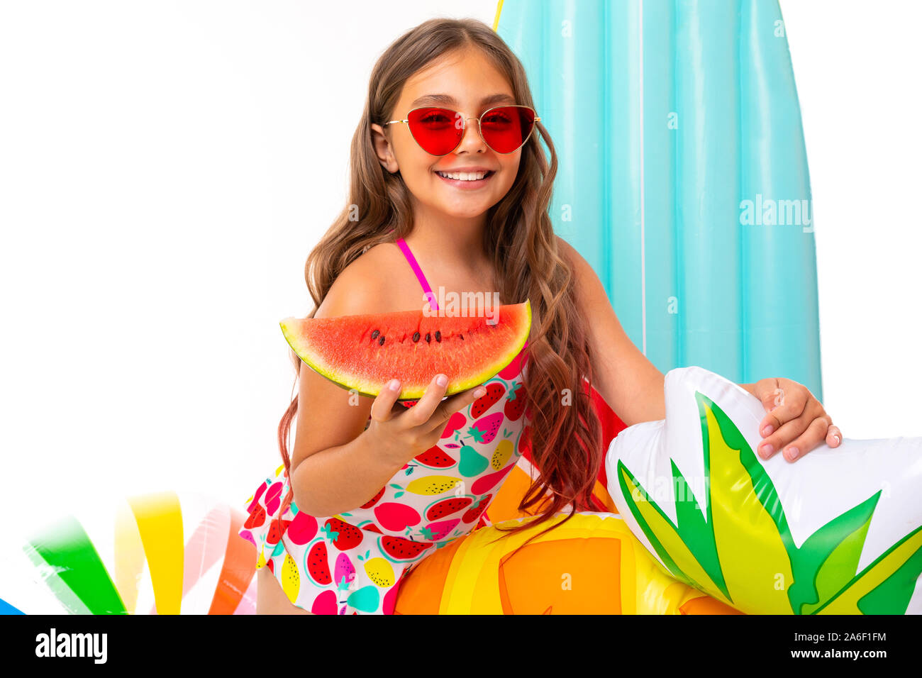 Mädchen mit langen gekreuzigt Haar in Sonnenbrille und Sonnencreme, steht in der Nähe von aufblasbaren Matratzen mit einer Wassermelone Stockfoto