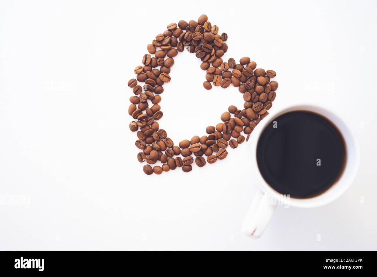 Herzform aus Kaffeebohnen mit Tasse Kaffee auf weißem Hintergrund. Ich liebe Kaffee Stockfoto