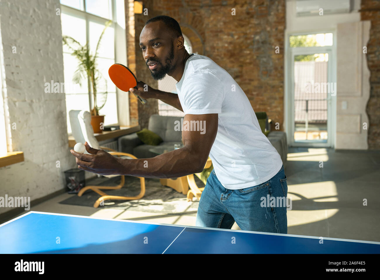 Junger Mann Tischtennis spielen am Arbeitsplatz, Spaß zu haben. Modell legere Kleidung spielen Ping pong zusammen an einem sonnigen Tag. Konzept der Freizeitgestaltung, Sport, Freundschaft, Teambuilding, Teamarbeit. Stockfoto