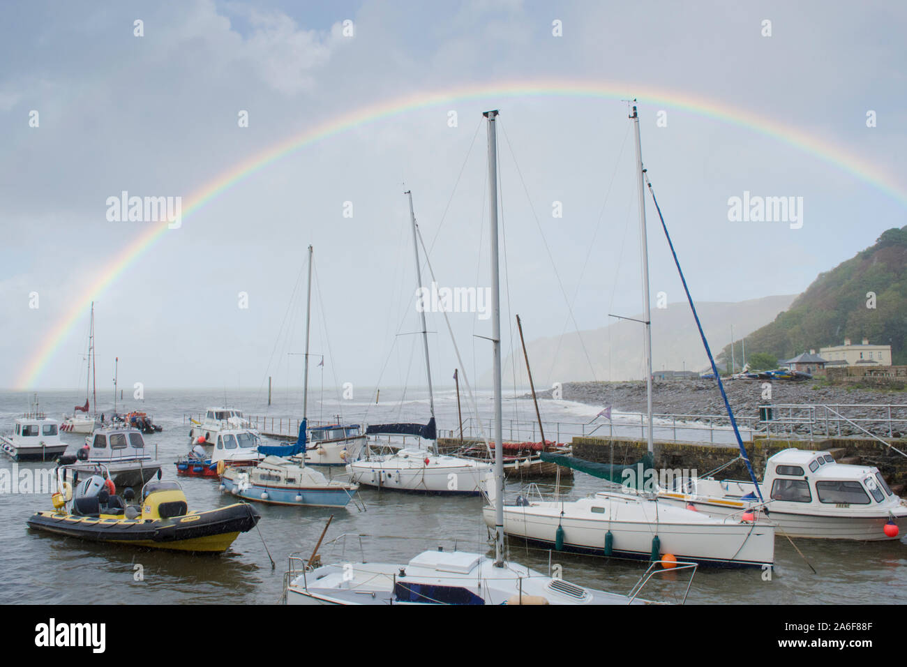 Regenbogen über dem Meer, Boote, Hafen und Strand in Lynmouth bei stürmischem Wetter, Devon, UK, September. Höhe Tide,, Stockfoto