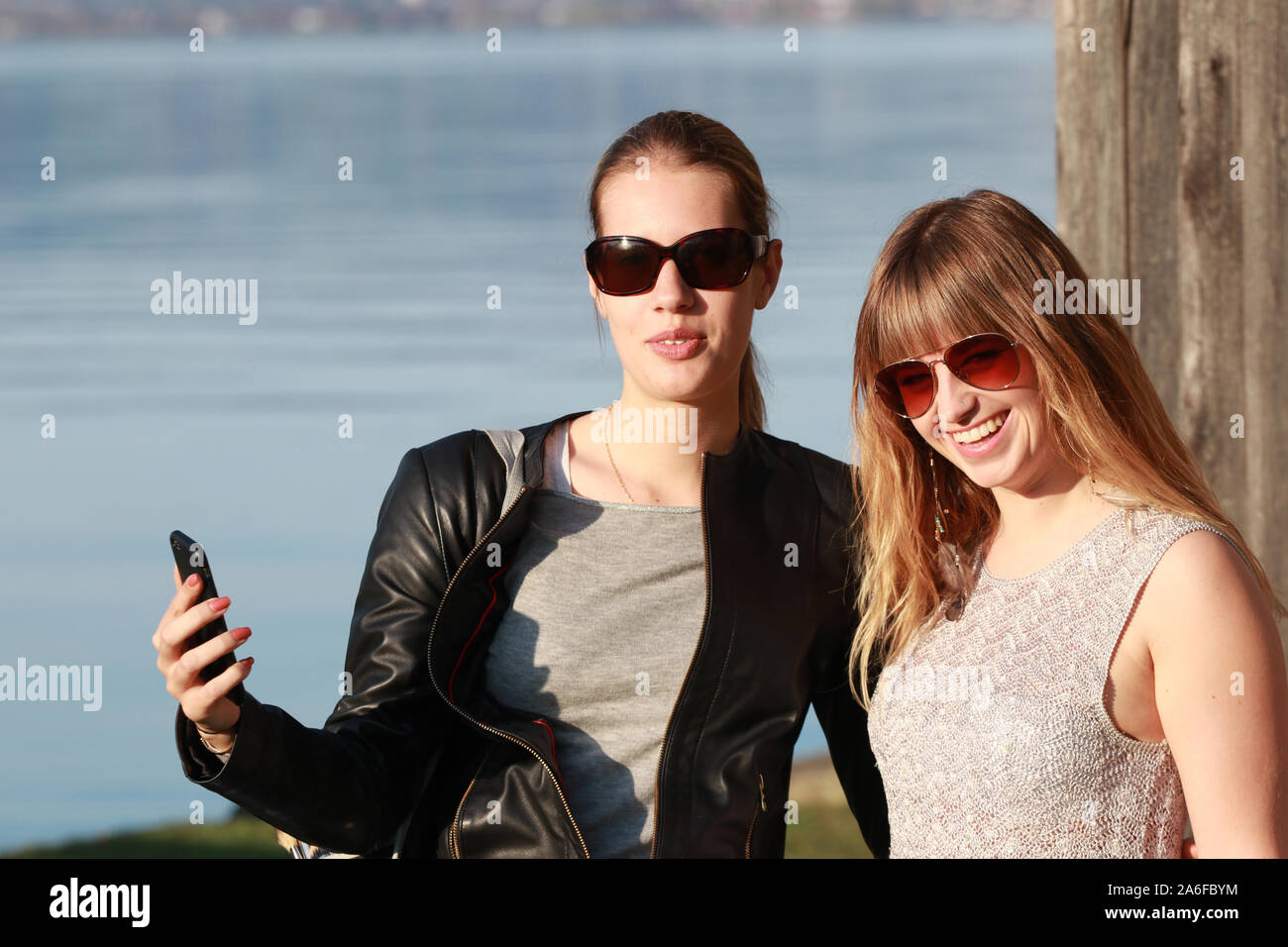 Zwei Mädchen mit Sonnenbrille am See selfies nehmen und Spaß Stockfoto