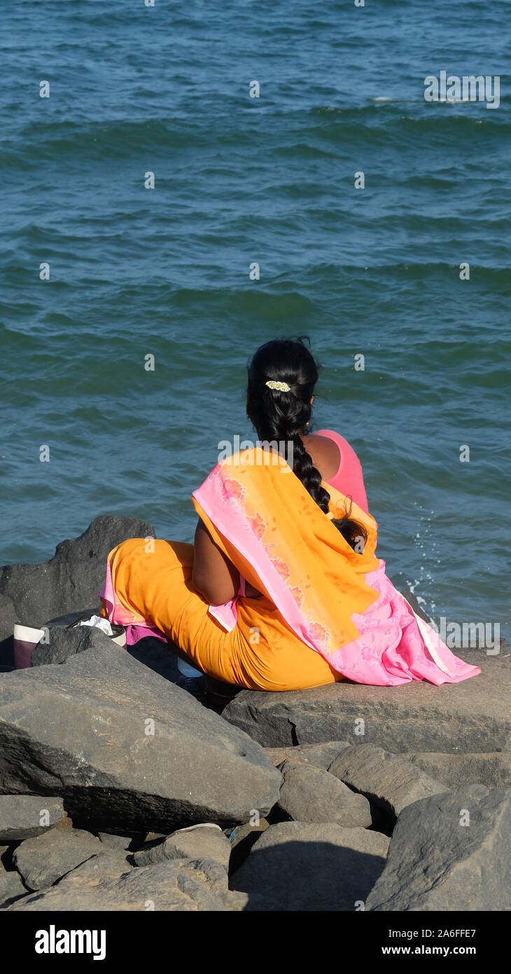 PONDICHERRY/INDIEN - 23. FEBRUAR 2018: Indische Frau im Sari sitzt auf einem Felsen und blickt auf das Meer. Stockfoto