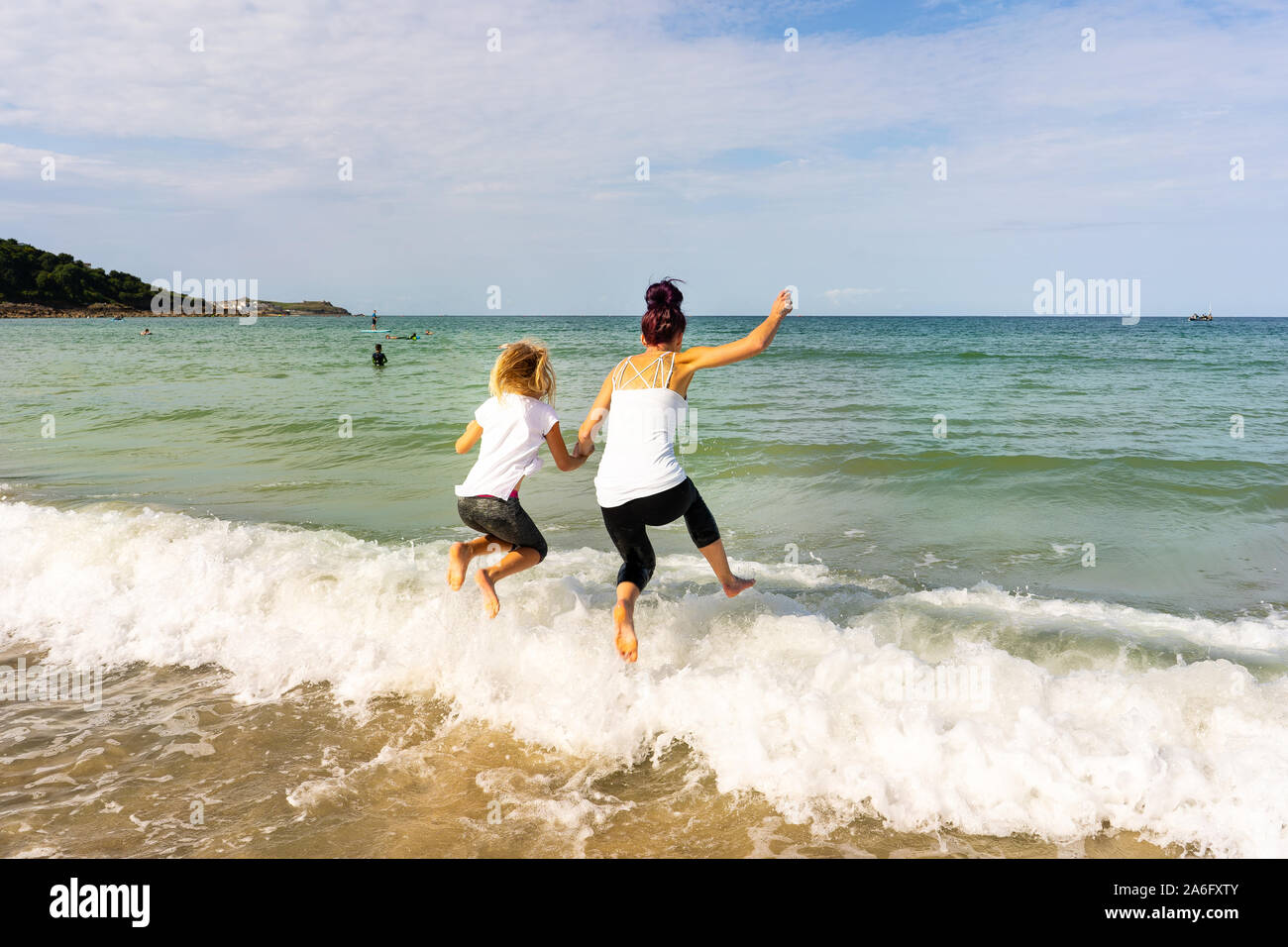 Mutter und Tochter verbringen die Zeit zusammen, Paddeln, Springen über die Wellen ins Meer an der wunderschönen St Ives in Cornwall Carbis Bay Stockfoto