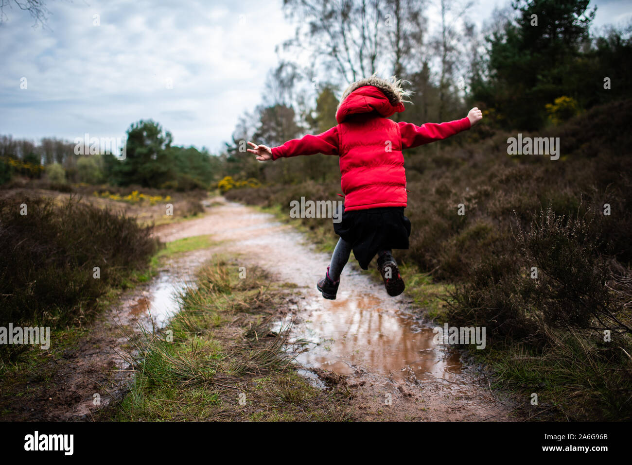 Ein kleines Mädchen geht, läuft und springt durch und in sehr schlammigen Pfützen auf dem Land auf einer Familie zu Fuß trägt einen warmen roten Körper wärmer Stockfoto