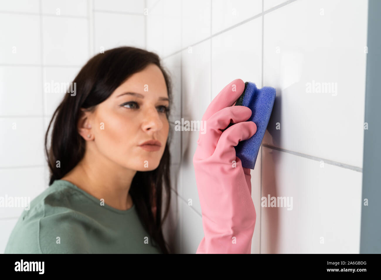 Junge Frau mit Schutzbrillen Reinigung Der weiße Fliesen der Wand mit Schwamm Stockfoto
