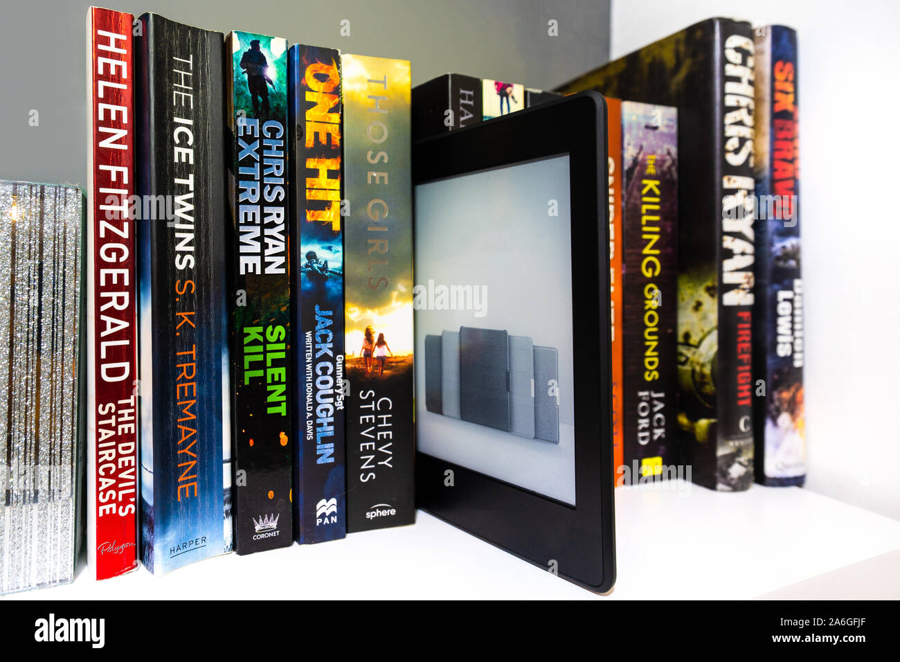 Ein Ereader Kindle voller Ebooks auf einem Bücherregal von anderen normalen Papier wieder Romane umgeben Alle darauf warten, gelesen zu werden. Das digitale Lesen vs Traditionelle. Stockfoto