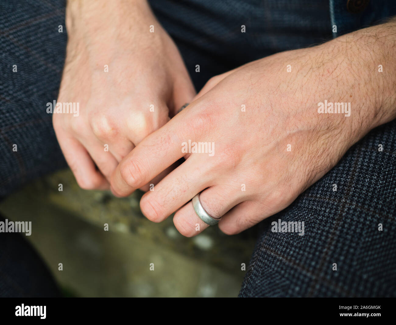 Junge Männer 20-25 Jahre isoliert Hände mit Ring am linken Ringfinger, Sitzen mit den Händen zwischen den Beinen. Kein Gesicht sichtbar. Stockfoto