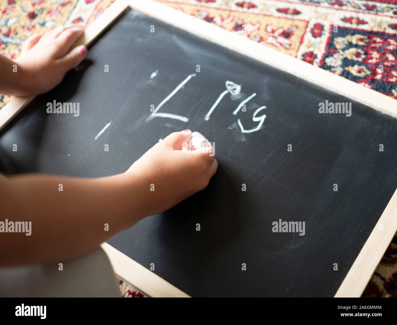 4-Jähriges Mädchen schreibt LilyI auf einer Schiefertafel, Teppich im Hintergrund. Stockfoto