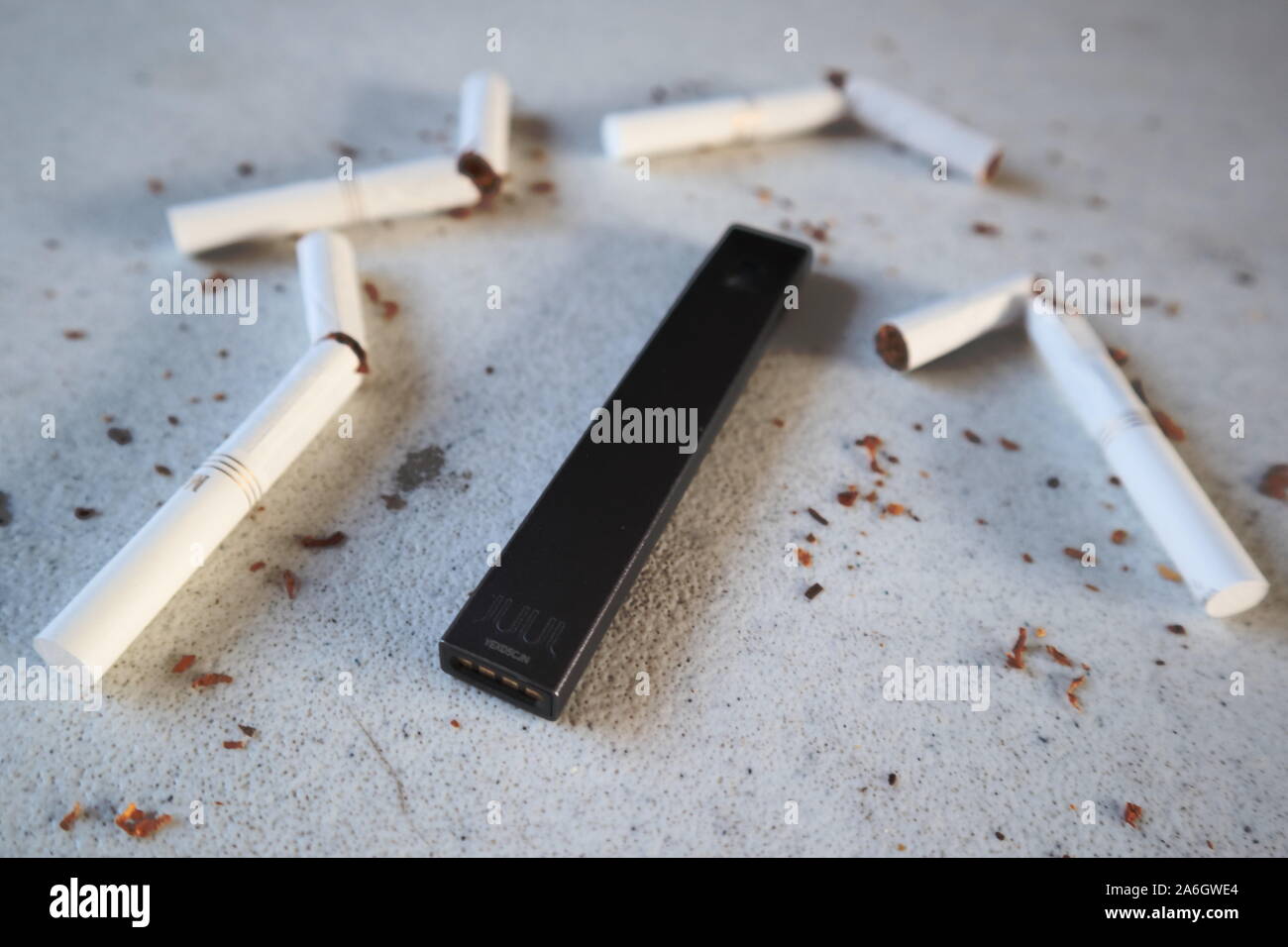 Vape Gerät Elektronische Zigarette Juul, wie Rauchen alternative mit gebrochenen Marlboro Gold Zigaretten und Tabak verstreut auf Weiß strukturierten Hintergrund Stockfoto