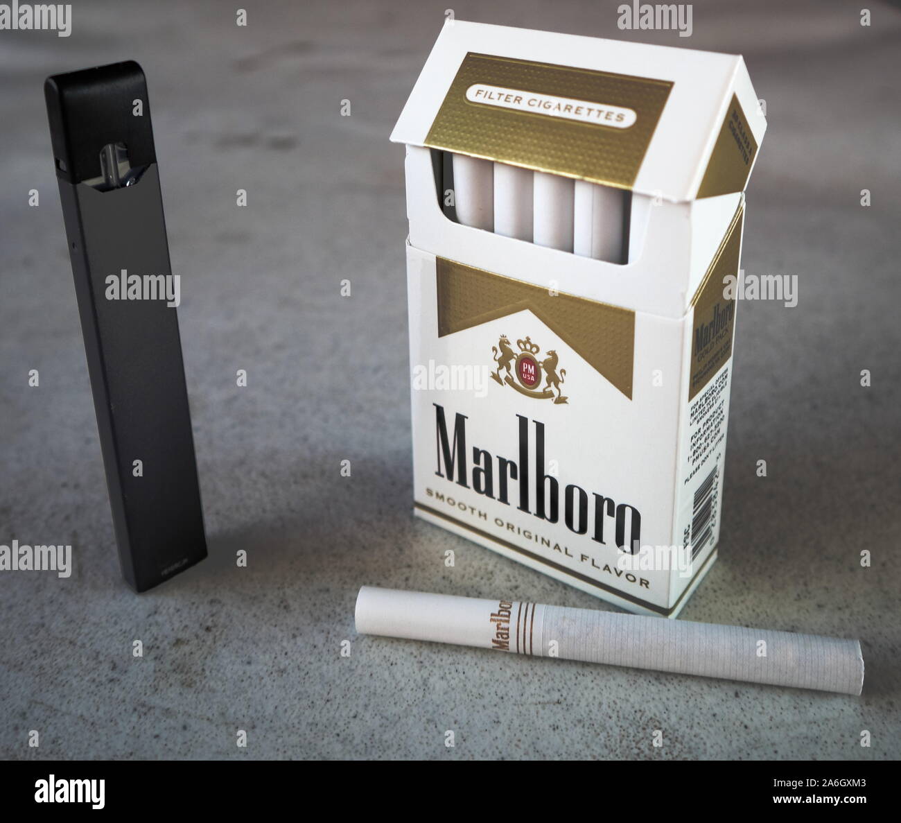 Juul vape Pod elektronische Zigarette Gerät mit einer Packung Marlboro Zigaretten und eine Zigarette draußen auf eine weiße strukturierte Tabelle gelegt, isoliert Stockfoto