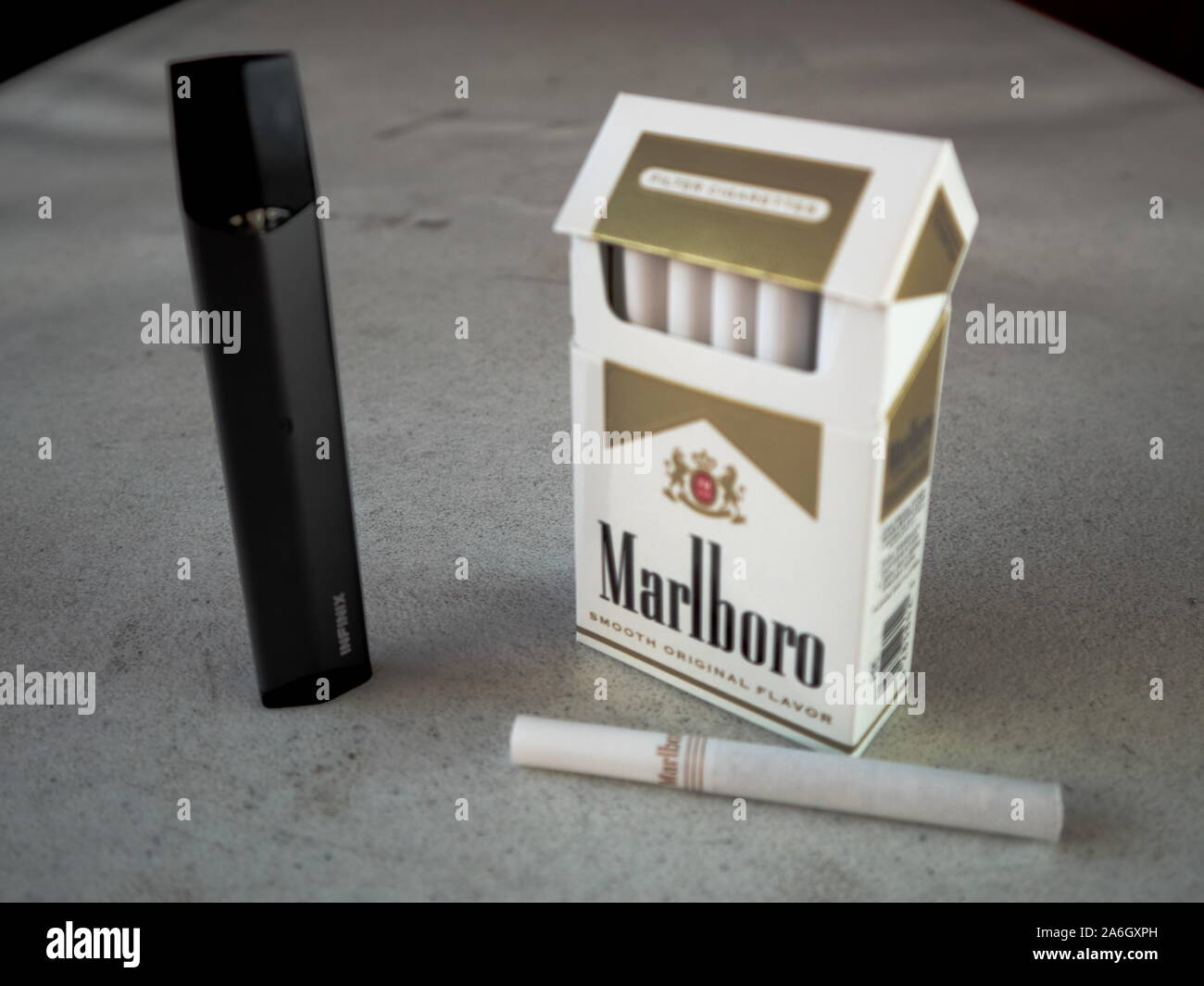 Smok infinix vape Pod elektronische Zigarette Gerät mit einer Packung Marlboro Zigaretten und eine Zigarette draußen auf eine weiße strukturierte Tabelle gelegt, Isola Stockfoto