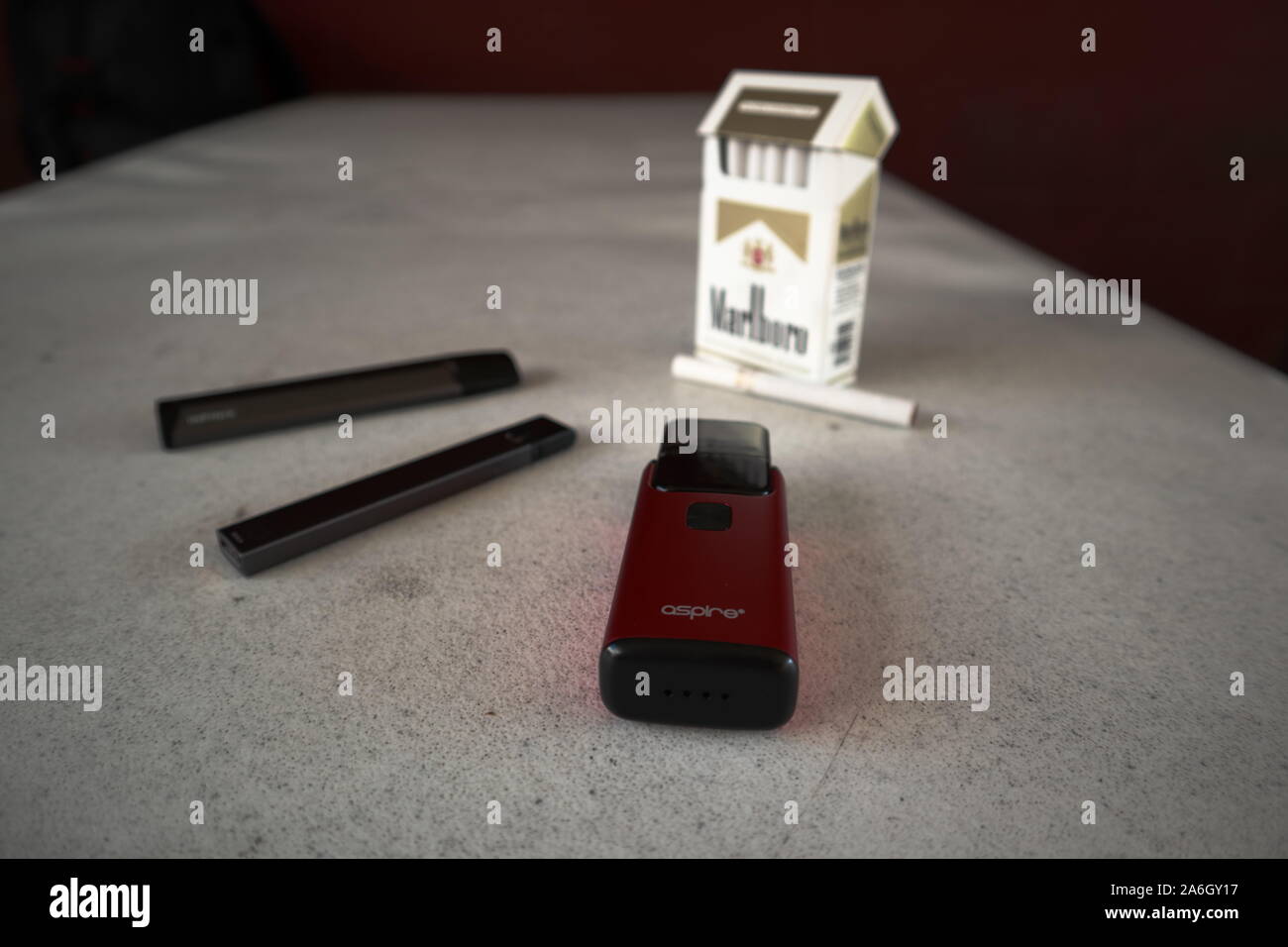 3 vapes Juul, Streben, Breeze, smok infinix mit einer Packung Marlboro Zigaretten und eine Zigarette draußen auf eine weiße strukturierte Tabelle gelegt, isoliert Stockfoto