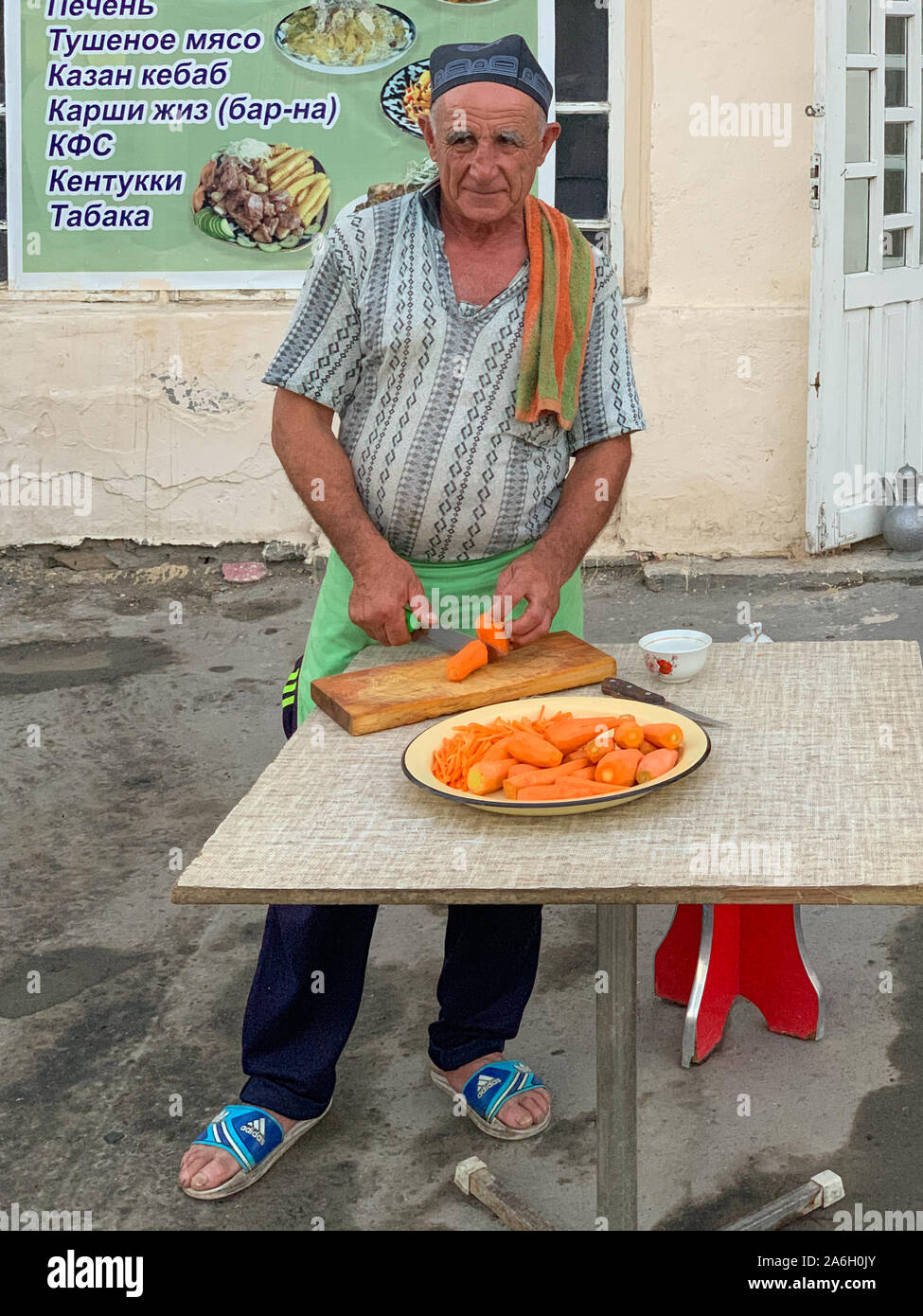 Buchara, Usbekistan - Juli 12, 2019: Alte Mann schneiden Karotten für Plov, die klassischen Usbekischen Gericht außerhalb. Stockfoto