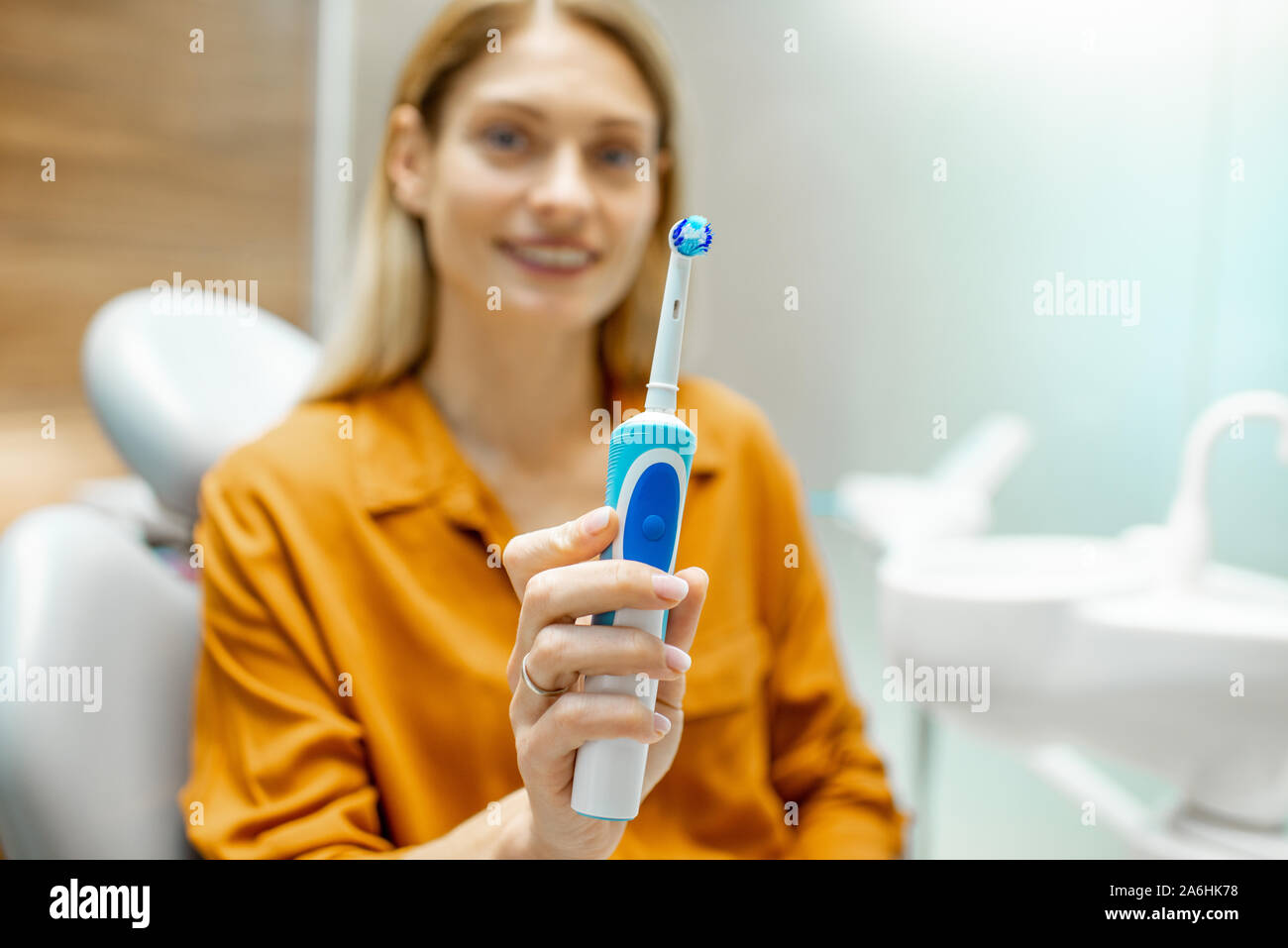 Porträt einer Schöne und fröhliche Frau als Patient mit elektrischen Zahnbürste sitzen auf dem Behandlungsstuhl im zahnmedizinischen Büro. Bild konzentrierte sich auf die Bürste Stockfoto