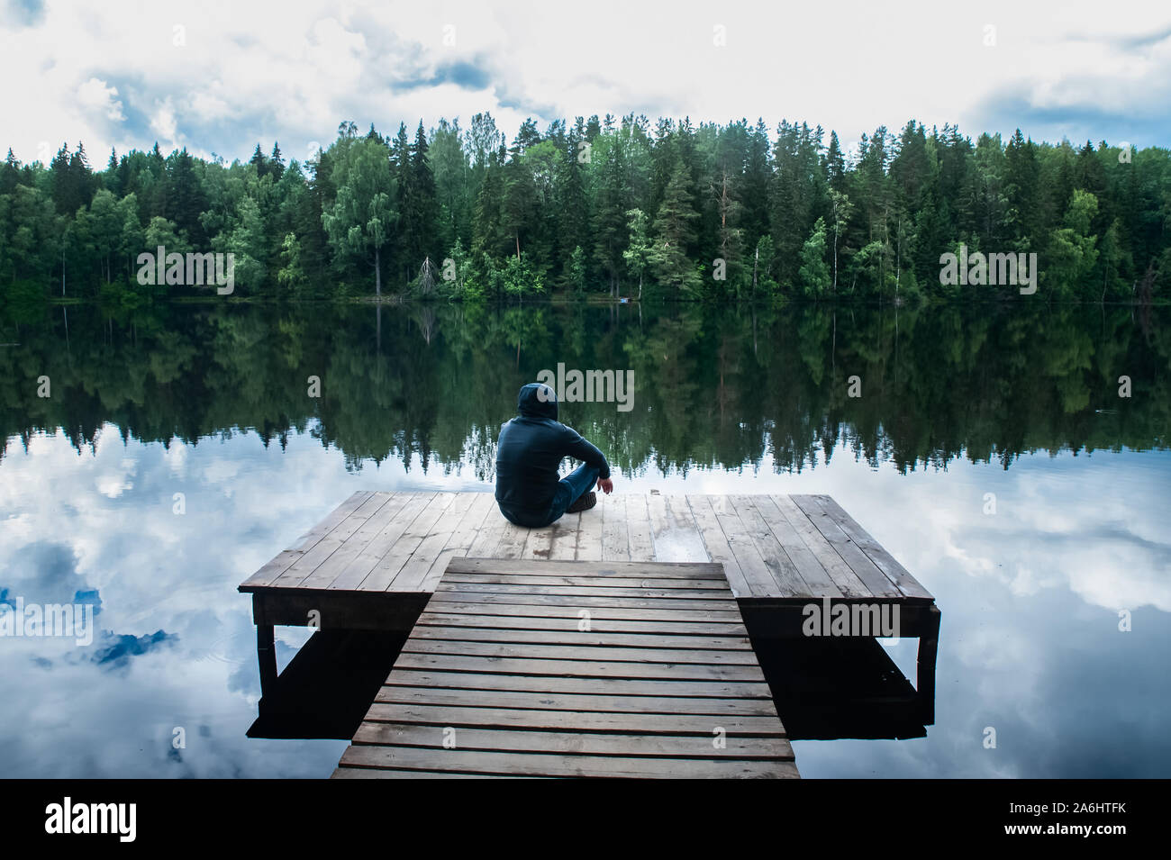 Mann sitzt auf dem Pier von einem schönen See. Der Begriff der Freiheit und Unabhängigkeit, ein symbolisches Foto von der Schönheit der Natur Stockfoto