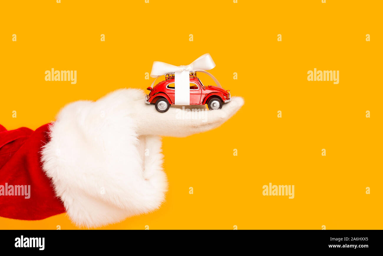 Santa Claus Holding modernes Auto mit Bogen in der Hand über Orange Stockfoto