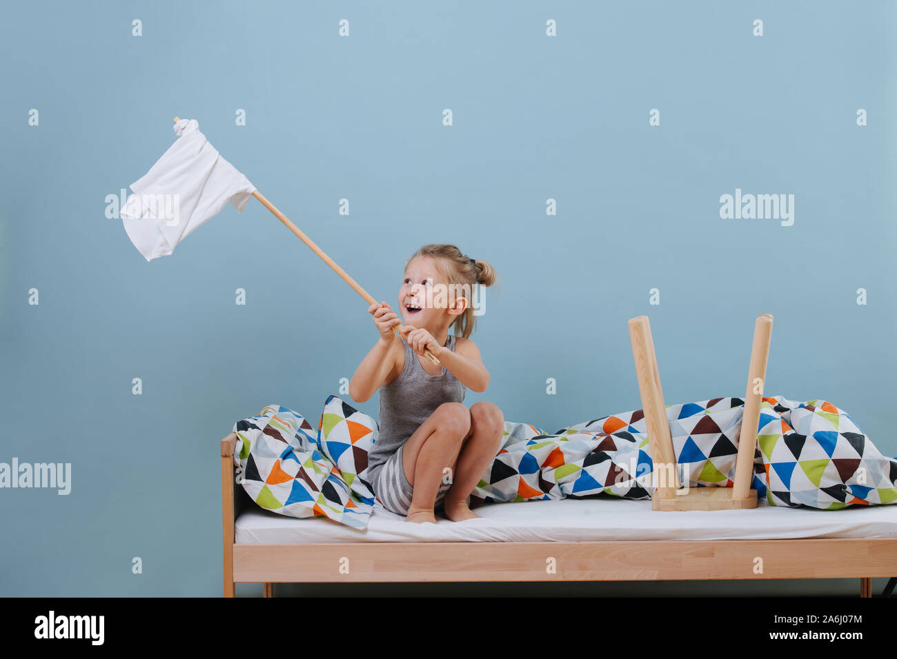 Kleiner Junge sitzt auf ungemachten Bett, wehenden weißen Flagge über blaue Wände Stockfoto