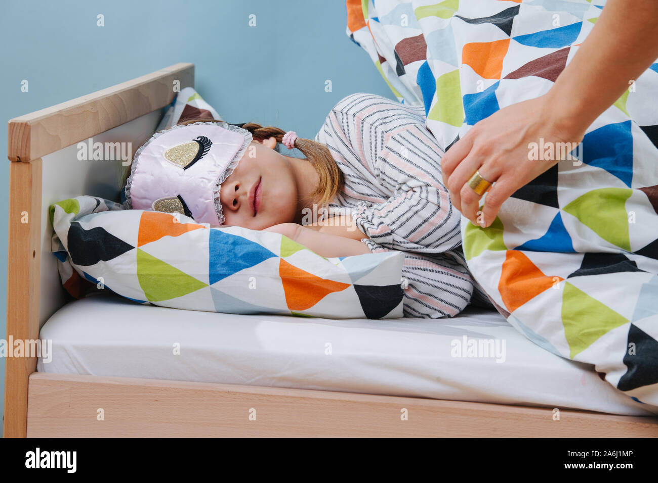 Mutter steckt ihre kleine Tochter im Bett. Mädchen mit schlafbrille. Stockfoto