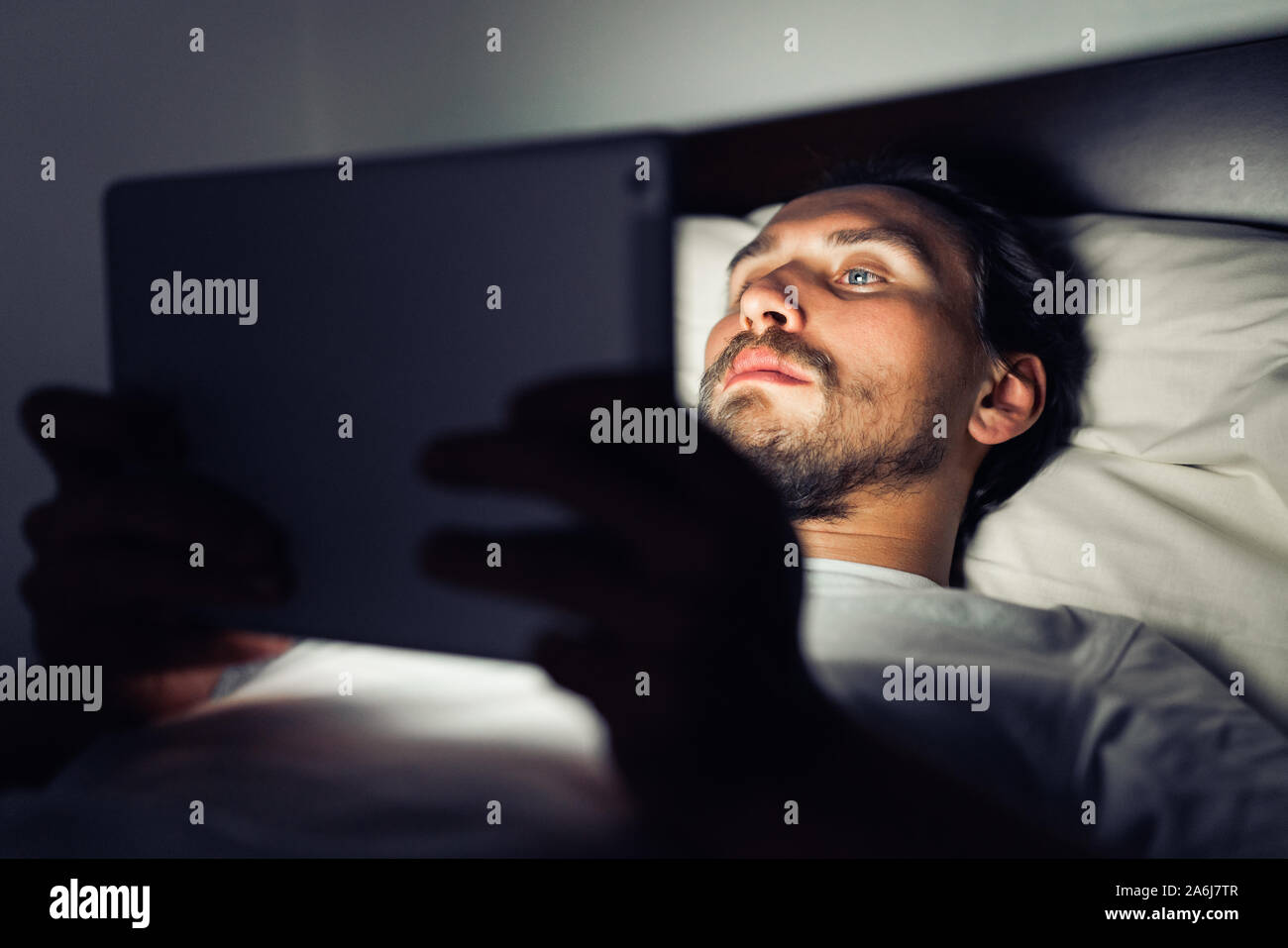 Junge stattlich und müde Mann mit einem Bart kann nicht schlafen und ist etwas aufpassen auf seinem Tablet in der Nacht. Stockfoto