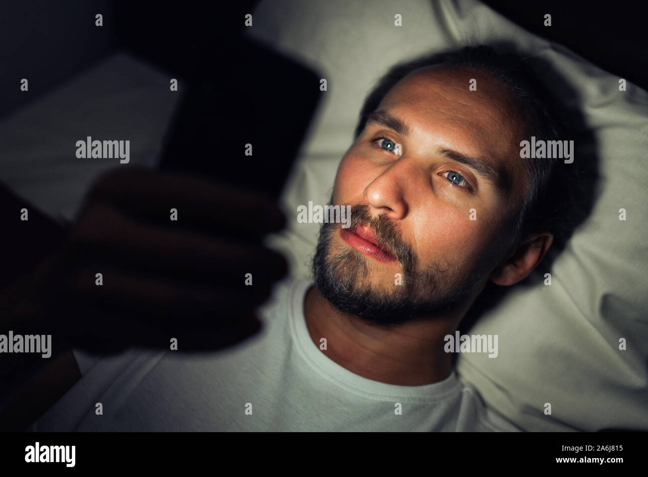 Junge stattlich und müde Mann mit einem Bart kann nicht schlafen und ist etwas aufpassen auf sein Handy in der Nacht. Stockfoto
