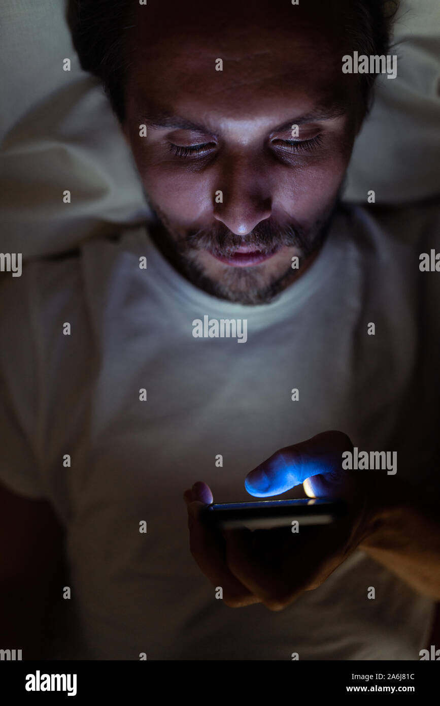 Junge stattlich und müde Mann mit einem Bart kann nicht schlafen und ist etwas aufpassen auf sein Handy in der Nacht. Stockfoto
