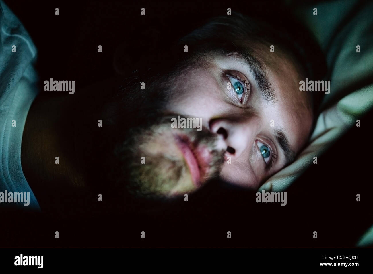Bärtige Kaukasier Männlich ist etwas aufpassen auf seinem Mobiltelefon nachts im Bett. Er ist eindeutig sehr müde, aber kann nicht schlafen. Stockfoto
